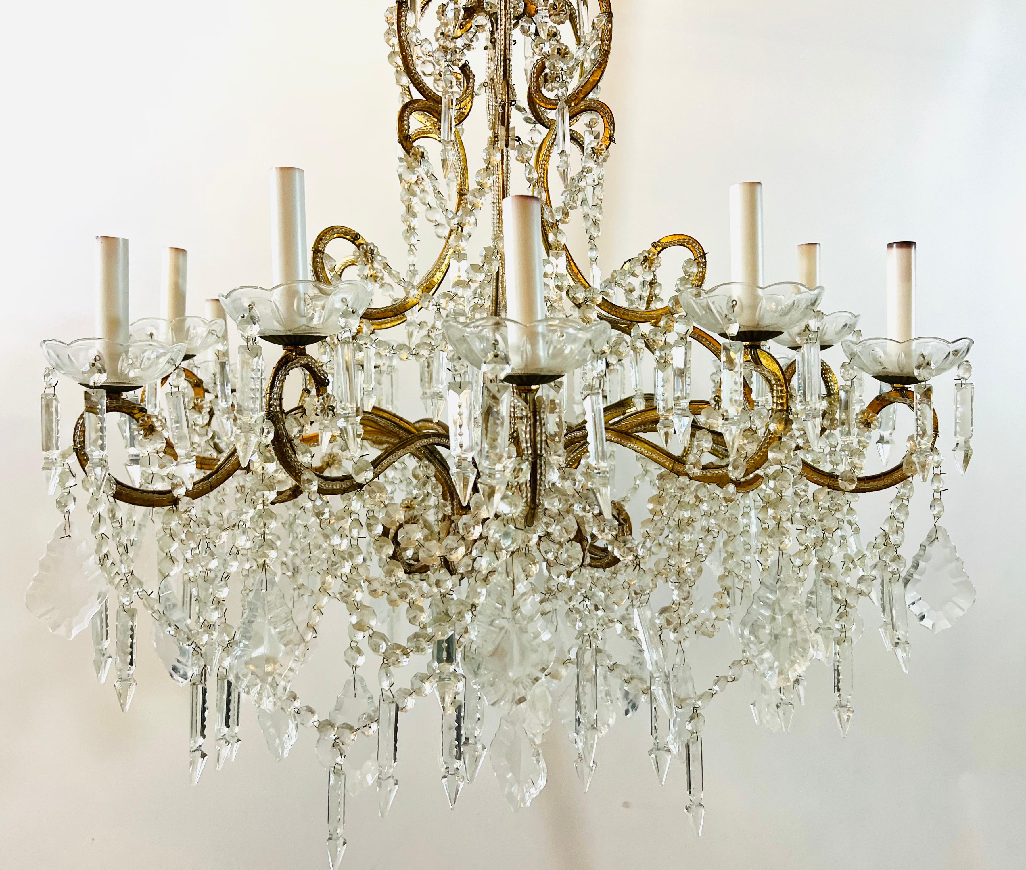 An elegant French Marie Therese Hollywood Regency style cut crystals 
chandelier having 12 arms. The multi-light chandelier is embellished with scrolls and gilt brass arms decorated with beads and French style pendaloques, obelisks crystals and
