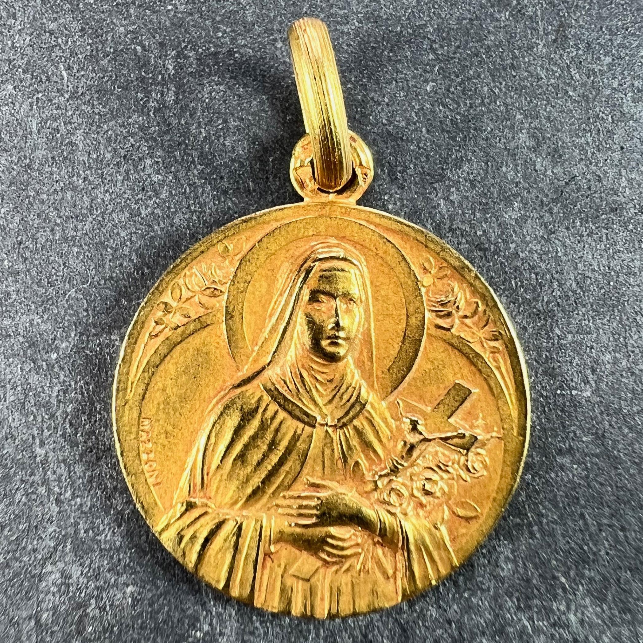 A French 18 karat (18K) yellow gold charm pendant designed as a medal depicting Saint Therese holding a crucifix and some roses, the surround with gothic detail. The reverse shows a wreath of roses, branches and leaves. Signed Mazzoni and stamped