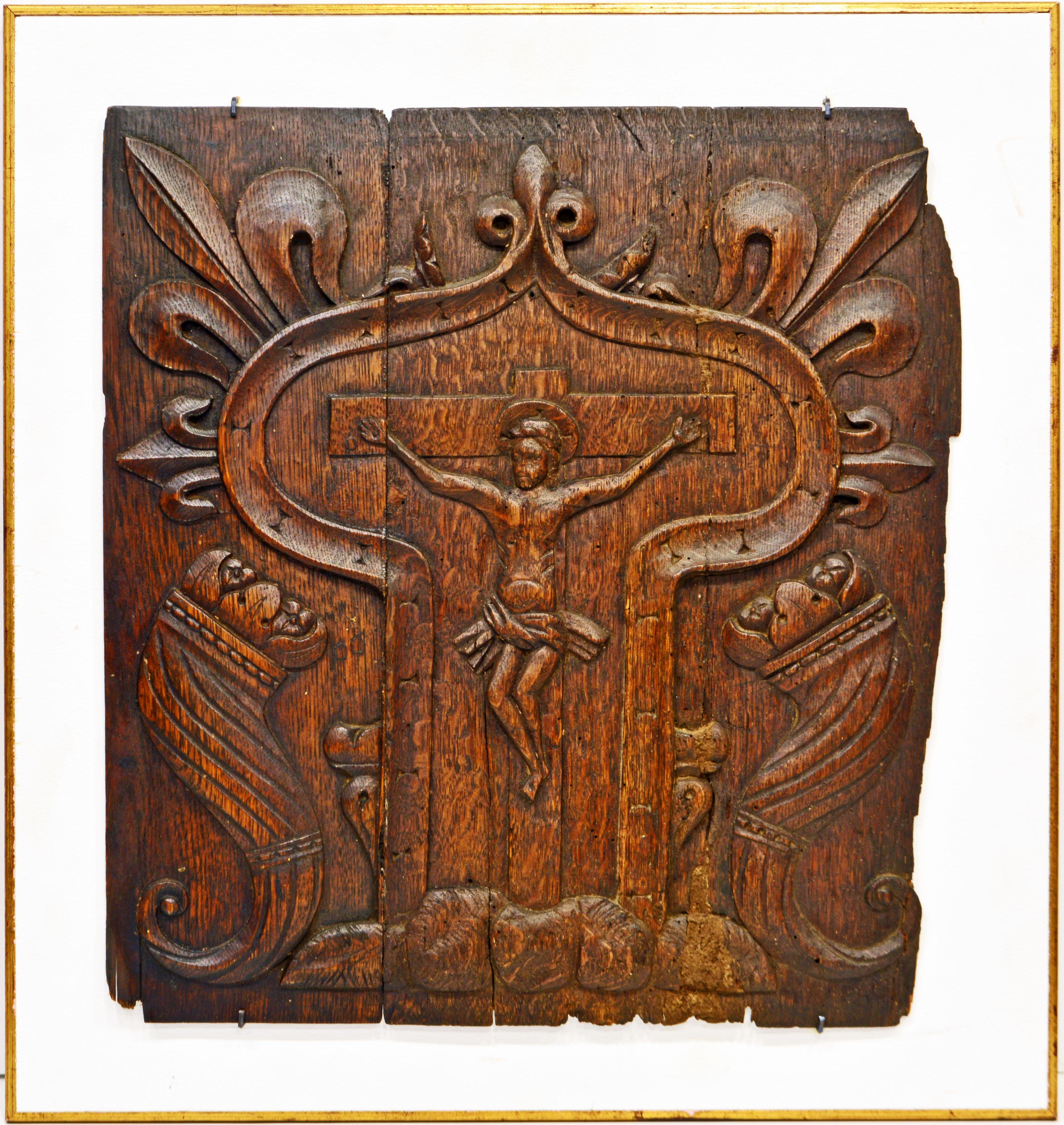 This medieval French relief carved oakwood panel depicts the crucified Christ flanked by two cornucopias and incorporated in a shaped border surmounted by the Fleur-de Lis symbol and radiating similar symbols. The carving is archaic in the