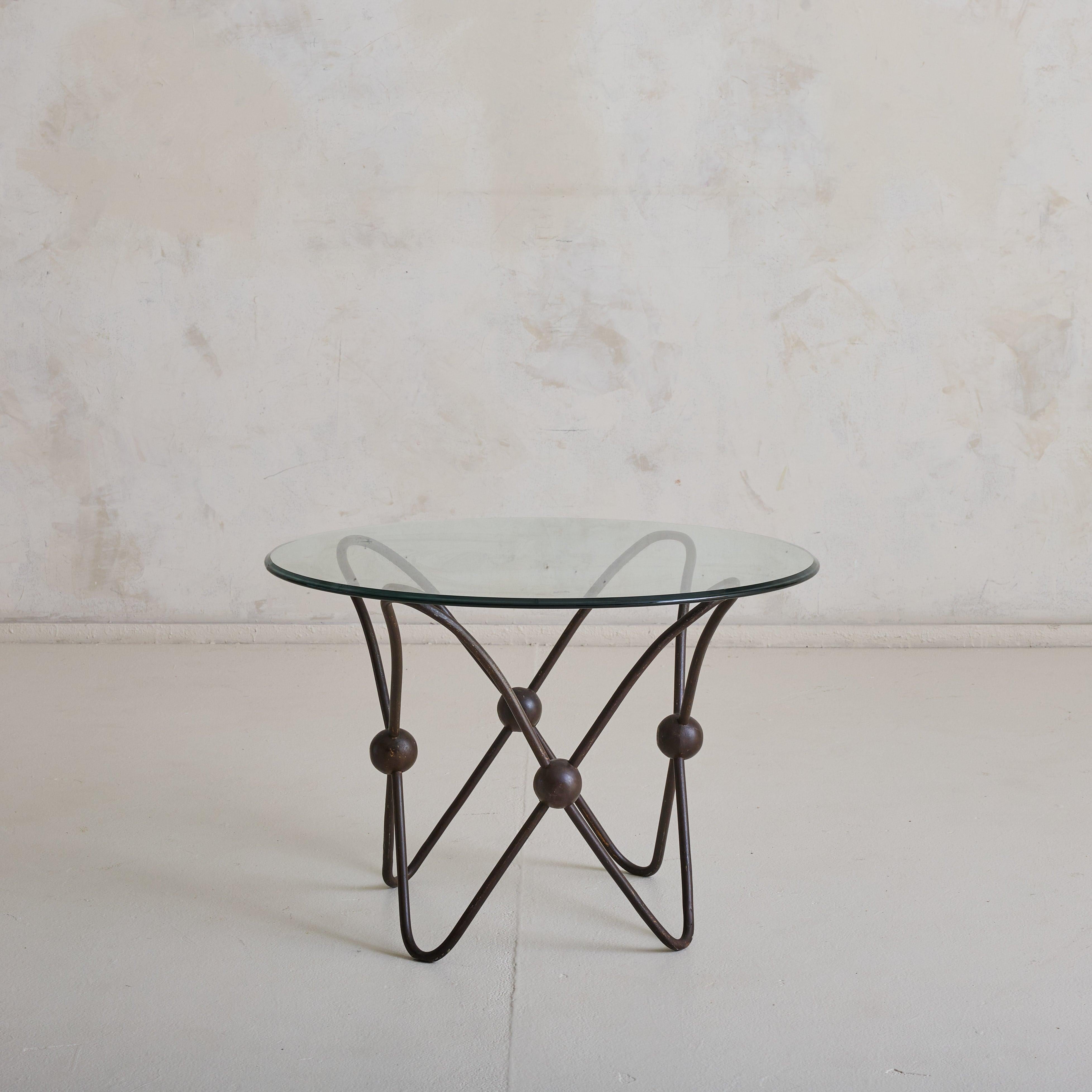 Une table basse française sculpturale des années 1950, qui incarne à la fois la force et la fluidité. Fabriquée en métal avec une finition patinée bronze, sa base ondulante est ponctuée de joints sphériques, créant un sens dynamique du mouvement et