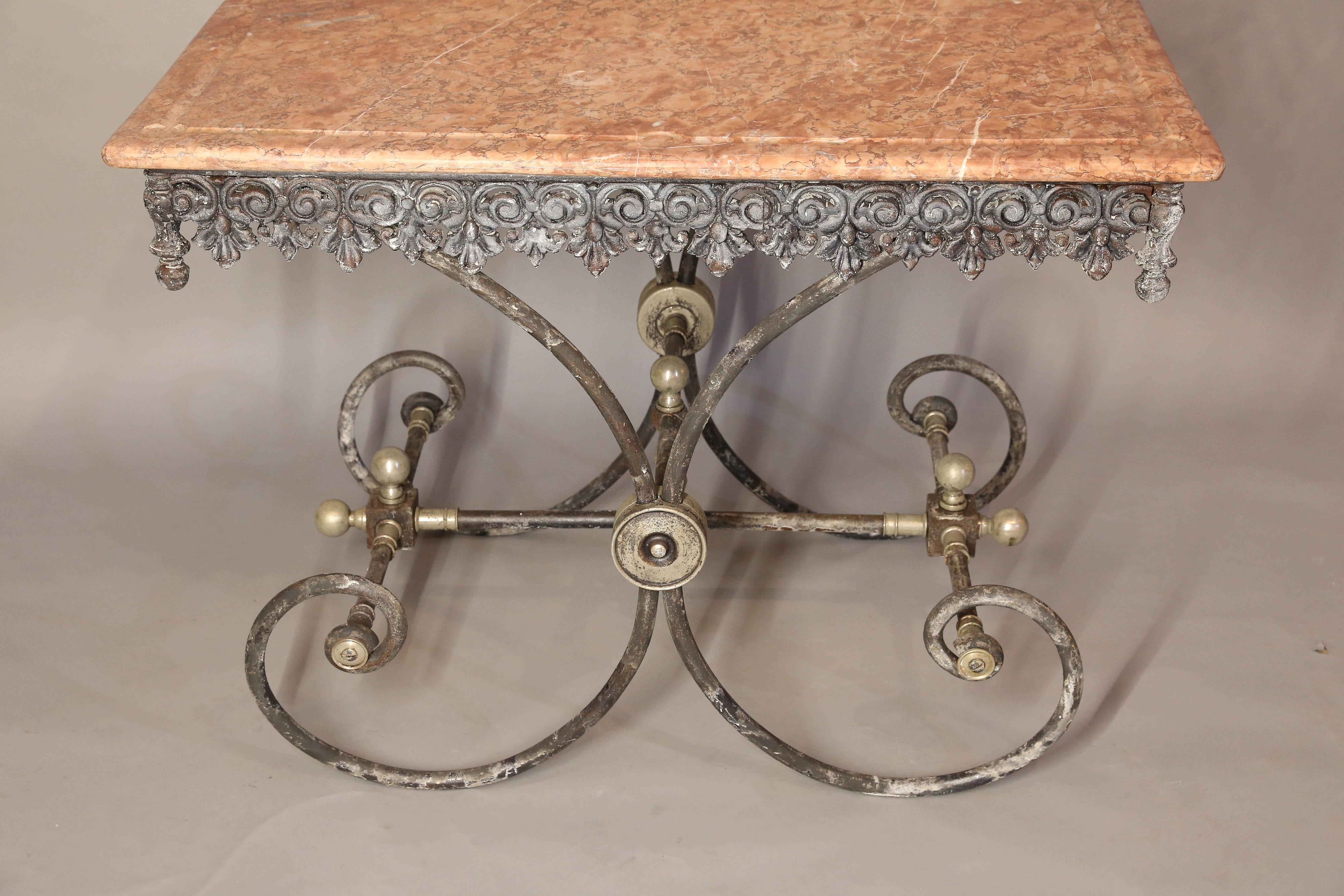 French pastry table has a decorative apron, rosettes and other decorative metal hardware on a scrolled base.
Marble top is Sienna color with a carved channel around perimeter. May have been used in butcher shop, for meat display.
 