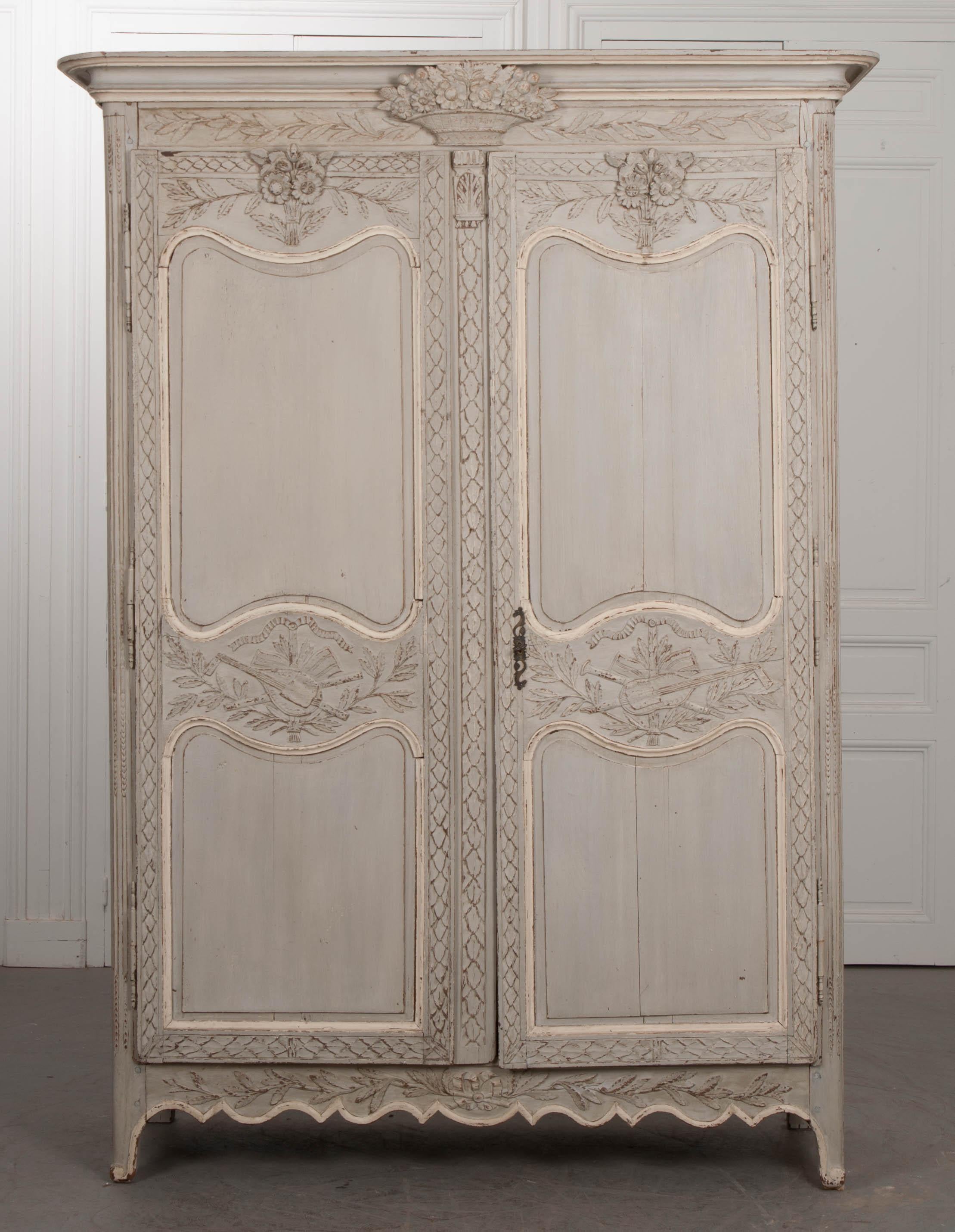 A French Louis XV to Louis XVI transitional dove-grey and ivory-painted oak marriage armoire, circa 1750. The cornice features an exuberantly carved wedding basket, flanked by foliage motifs along the rail. The doors, having two shaped and recessed