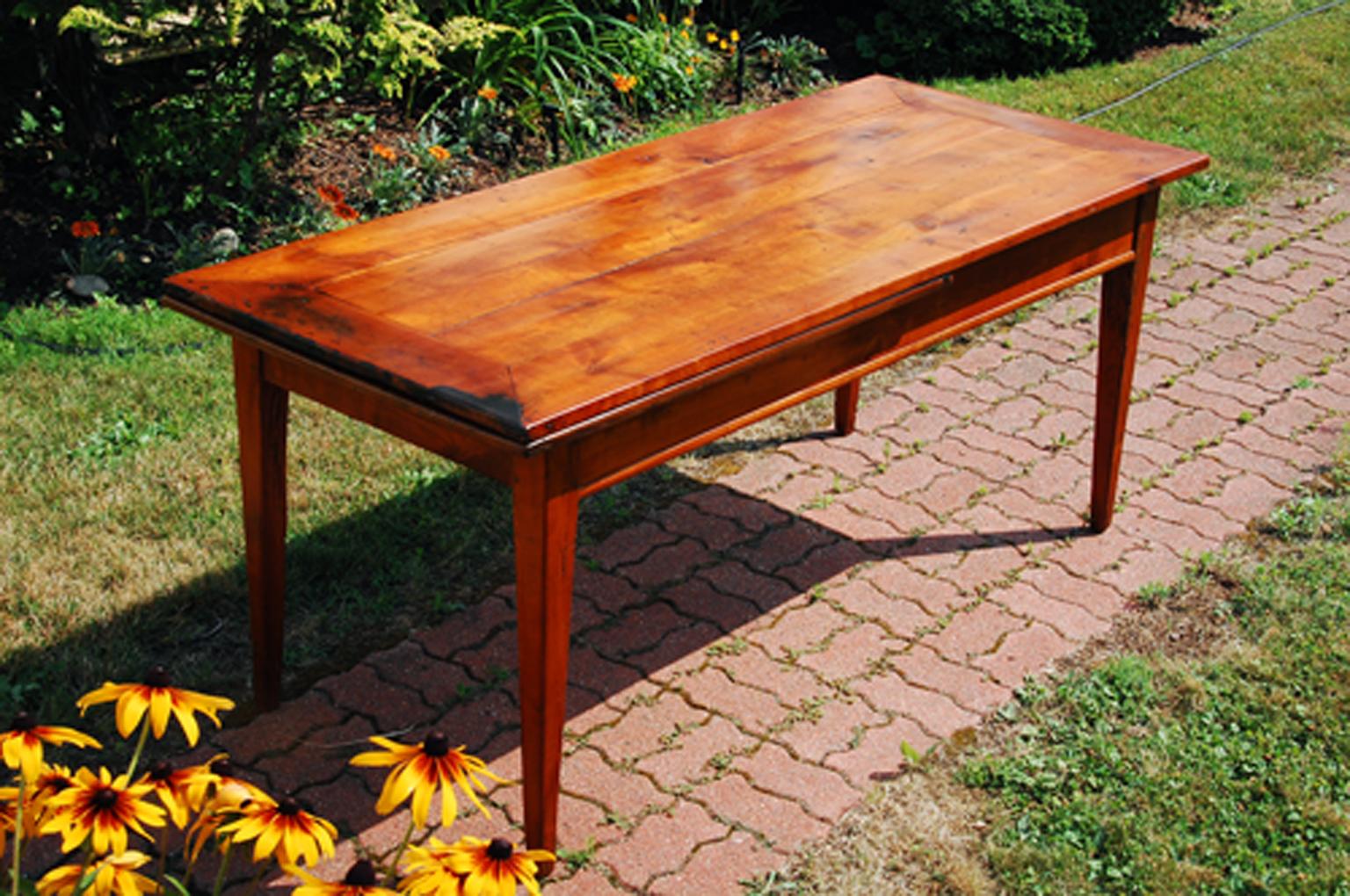 French provincial cherry mid 19th century farmhouse table.  This seventy two inch long taper leg table has a chestnut breadboard which slides out from one long end of the table for an additional twenty three inches of length.  It can be used not
