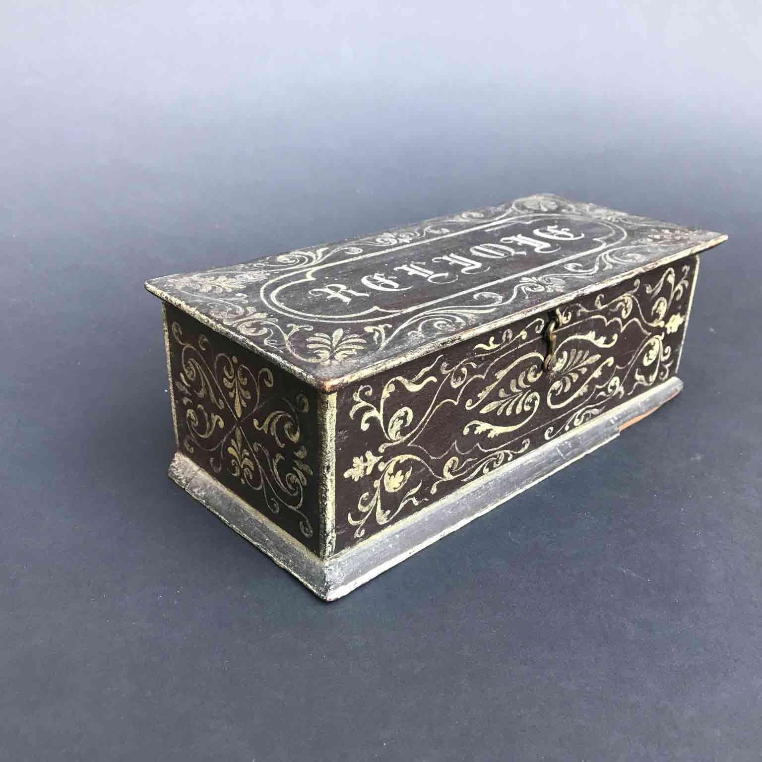 French 19th century lacquered rectangular shaped reliquary box, realized in oak, decorated with a dark brown/grey lacquering and a white scrolling and palmette pattern.
The lid shows the Gothic inscription Reliqie and closes with a hook. Blue