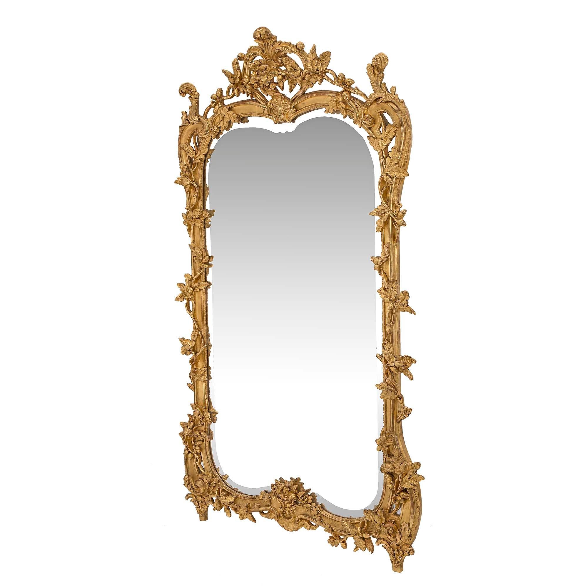 A stunning French mid-19th century Louis XV style giltwood mirror. The original beveled mirror plate is framed within a striking mottled giltwood border. The border displays a branch design and finely carved oak leaves with charming detailed acorns