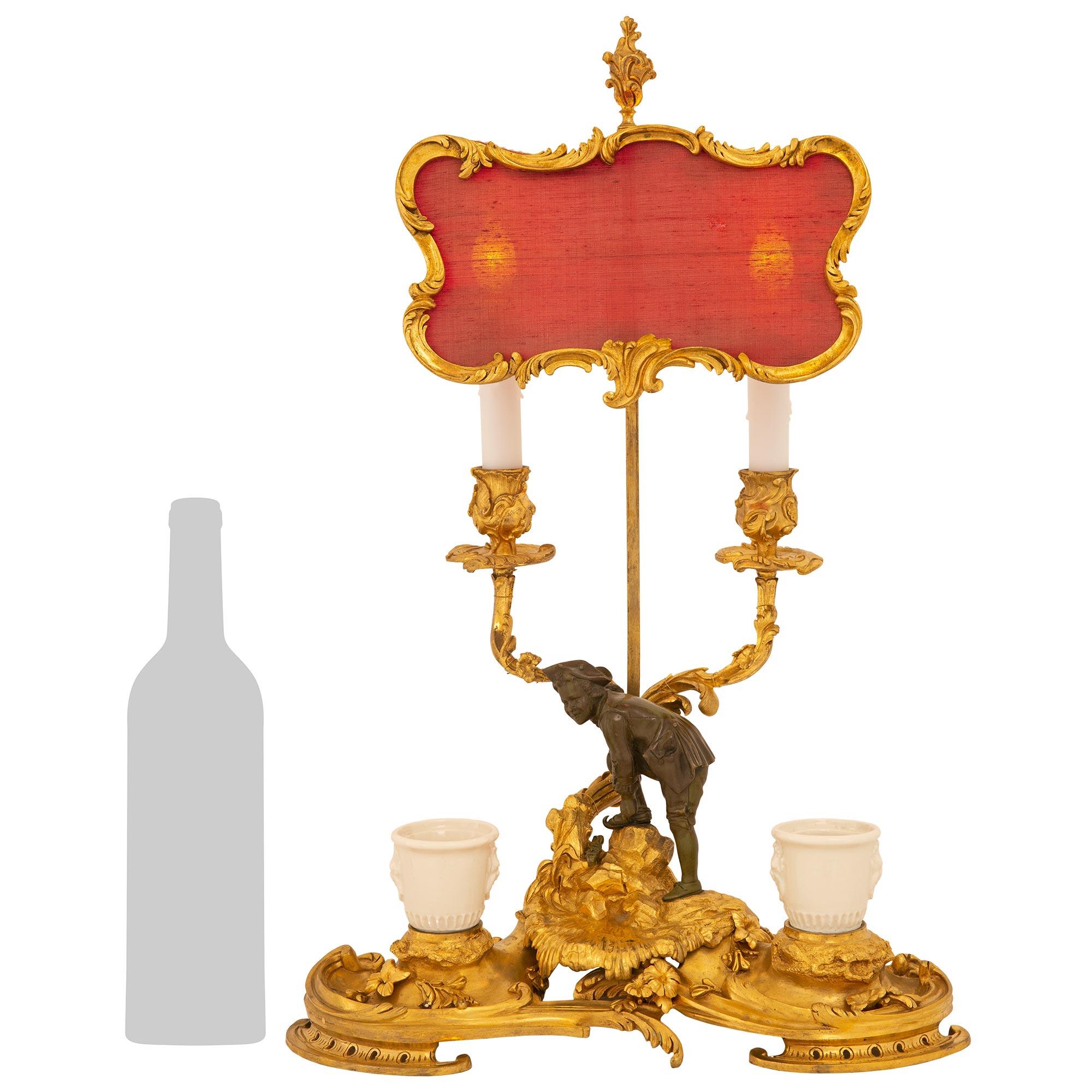 A unique and elegant French mid-19th century Louis XV st. ormolu candelabra lamp, with inkwells and adjustable screen. The lamp is raised by a kidney shaped base with satin and burnish finish displaying the original Blanc de Chine porcelain