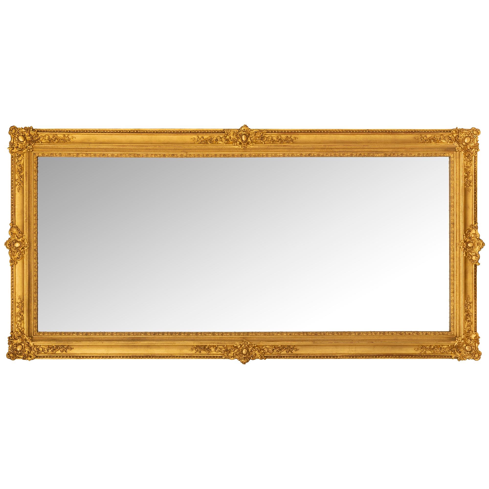 An elegant French mid 19th century Louis XVI st. Giltwood mirror. The mirror retains its original mirror plate framed within an elegant wrap around mottled border and a beautiful inner dentil moulding. The frame displays remarkable richly carved