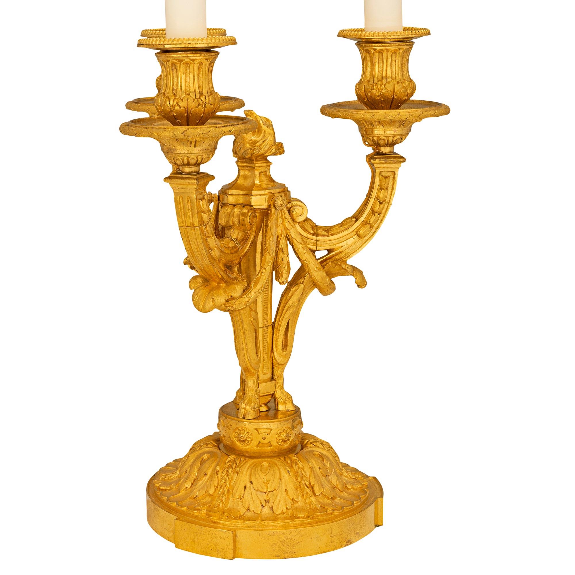A pair of exceptional French mid 19th century Louis XVI st. ormolu three light candelabra lamps. Each richly chased lamp is raised on a round base with acanthus leaves. The C scrolled arms decorated with laurel garlands, scrolls and acanthus leaves,