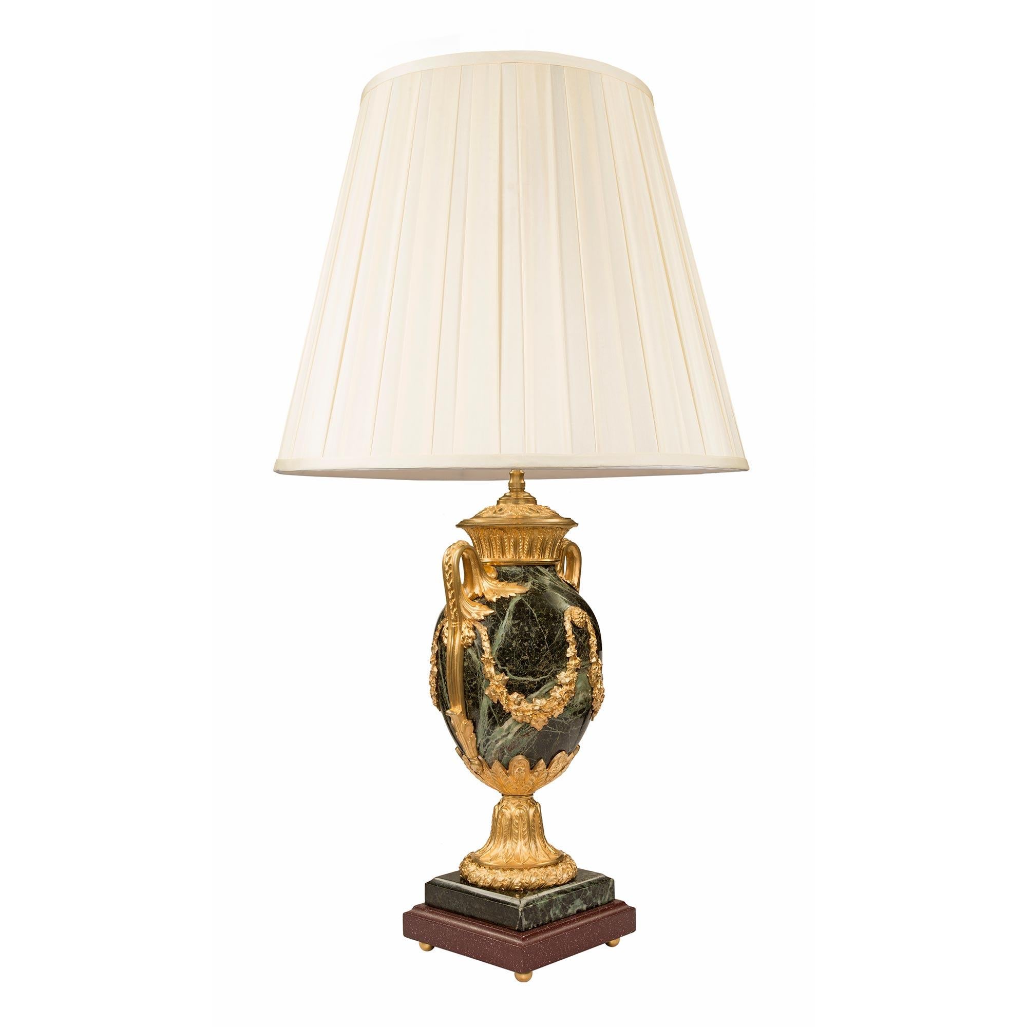 A very high quality French mid 19th century Louis XVI st. single lamp in ormolu, marble and faux porphyry. The lamp is raised by a square mottled edged faux porphyry base with ormolu ball feet. Above is the square Vert de Patricia marble plinth a