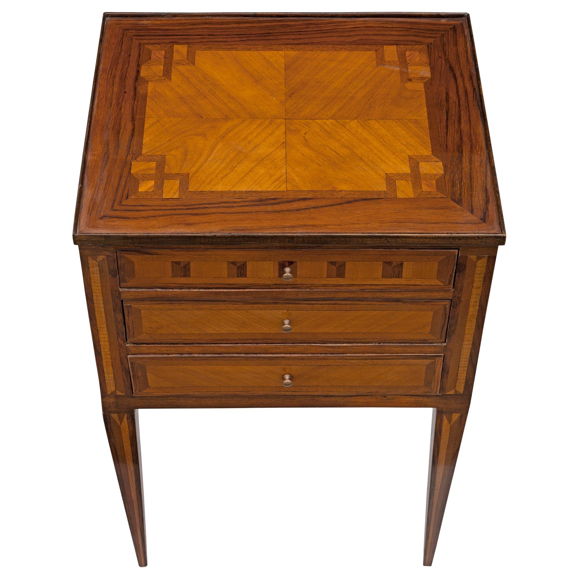 An elegant small scale French 19th century Louis XVI st. tulipwood and kingwood side table / chest. The table is raised by slender square tapered legs decorated with beautiful inlaid designs. At the center are three drawers with lovely butterfly