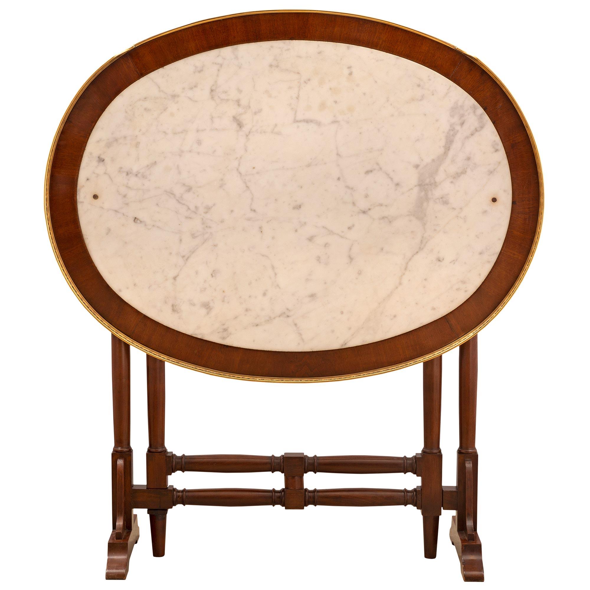 An elegant French mid 19th century Louis XVI st. mahogany, ormolu, and white Carrara marble gateleg table. The oval shaped table is raised by beautifully turned legs with arched supports at each side and elegantly curved elements. Each outer support