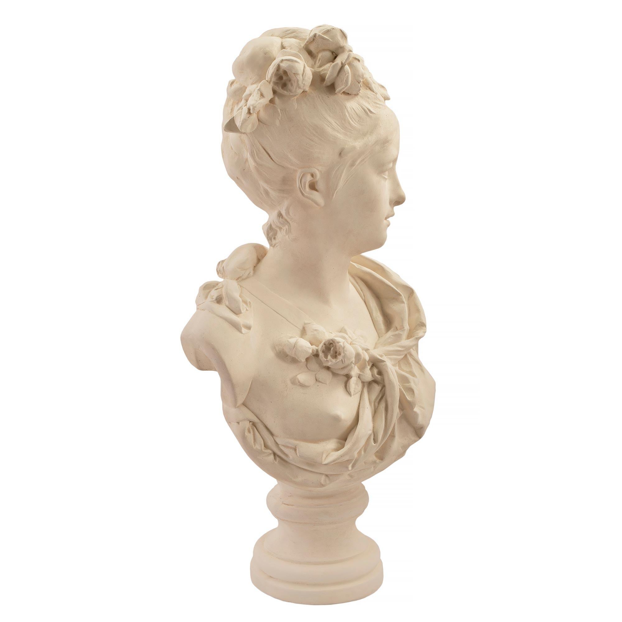 An elegant French mid-19th century plaster bust of a young lady, signed Albert-Ernest Carrier Belleuse. The bust of a young lady in classical attire accented with a small bouquet of flowers. She is wearing her hair in an updo decorated by row of