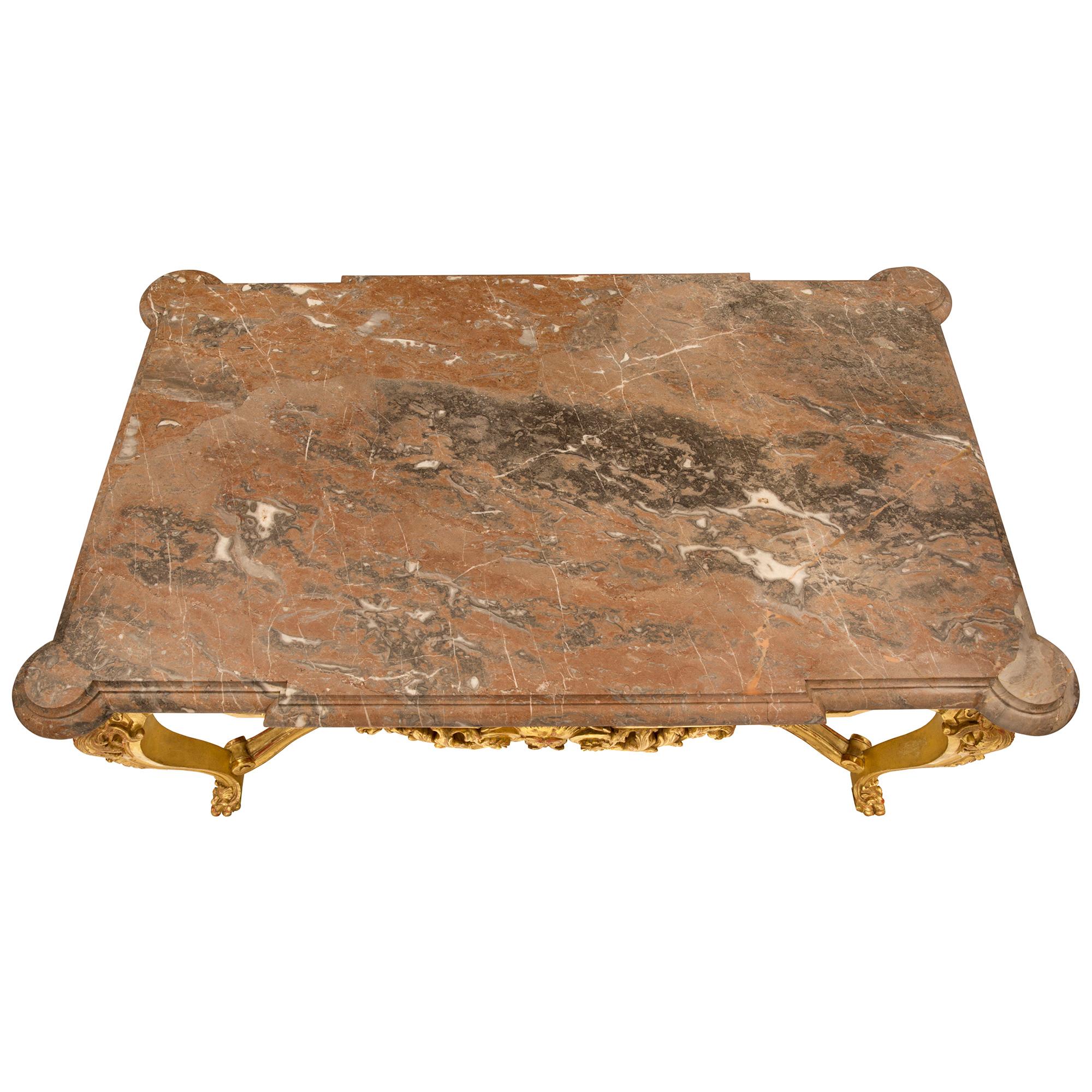 A spectacular French mid 19th century Régence st. giltwood and Rose Vif des Pyrenées marble center table. The rectangular table is raised by handsome paw feet with acanthus leaves below elegant cabriole shaped tapered legs adorned with richly carved