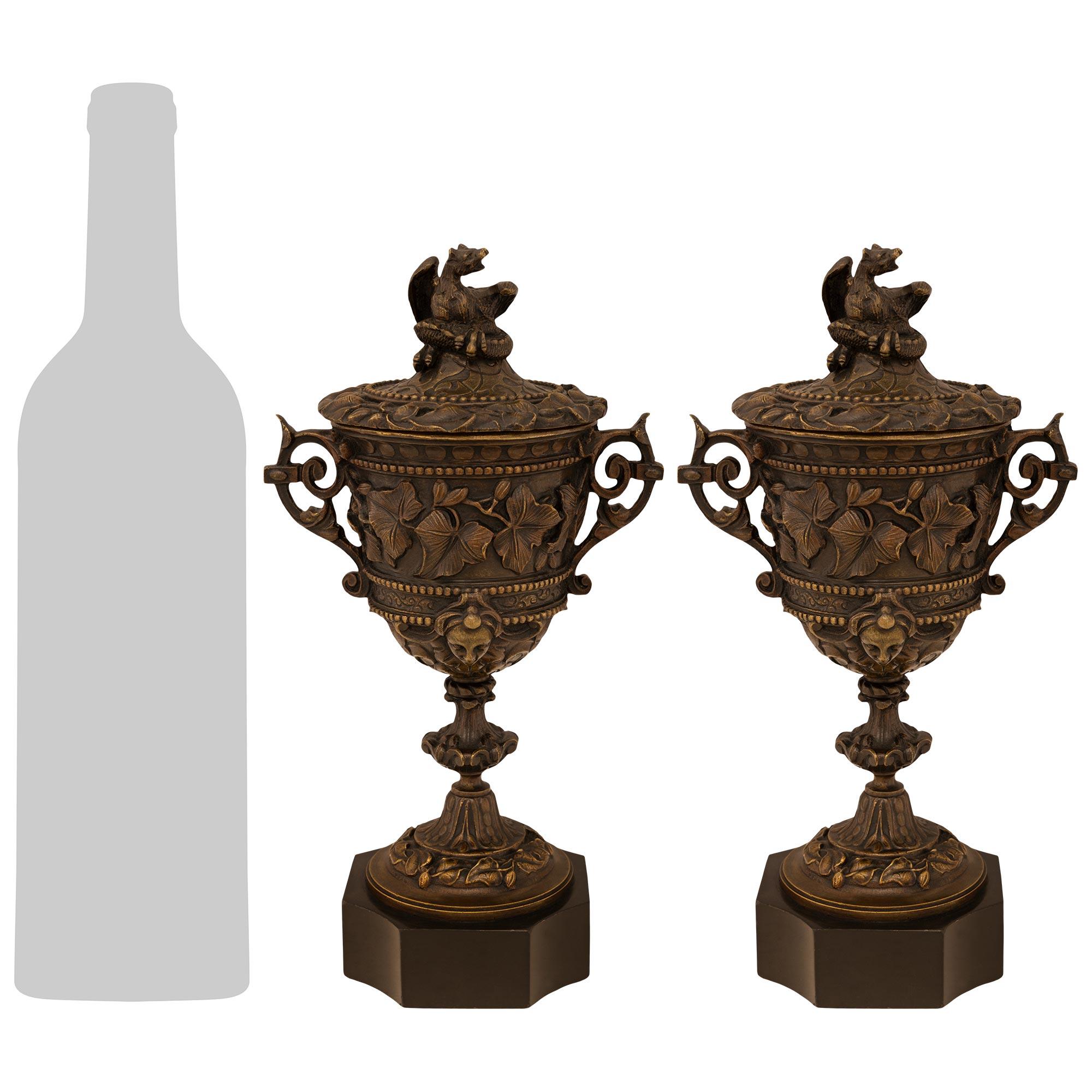 Una bella e decorativa coppia di urne con coperchio in bronzo patinato e marmo nero belga della metà del XIX secolo. Ogni urna è sollevata da una base quadrata in marmo belga nero con angoli concavi. Sopra c'è un supporto a socle meravigliosamente