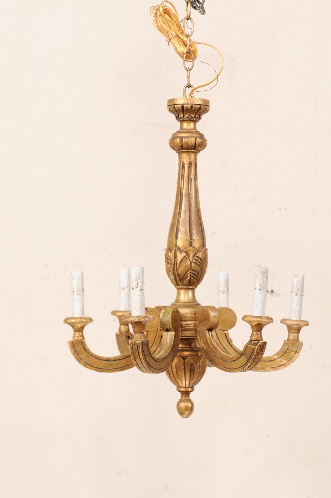 A French six-light carved and gilt wood chandelier from the mid-20th century. This vintage chandelier from France features a curvy central column, with fluted details, leaf motif carvings, and bottom finial. Six c-shaped arms, adorn the perimeter of