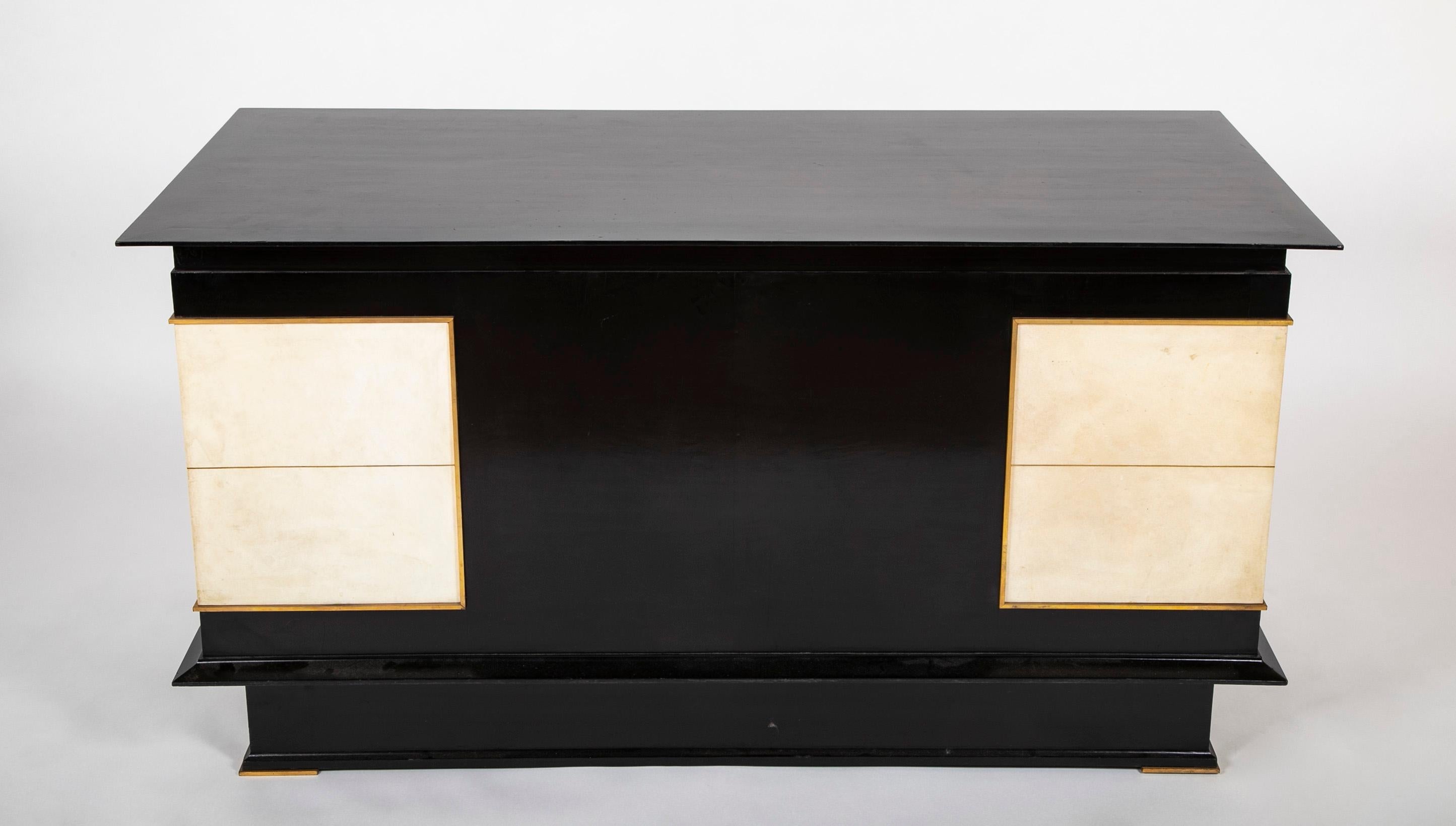 French mid-20th century seven drawer kneehole desk with a black lacquered finish inset with bronze framed cream-white parchment panels on the corners wrapping around from back to front. Bronze mounts on the feet and escutcheons, with five original