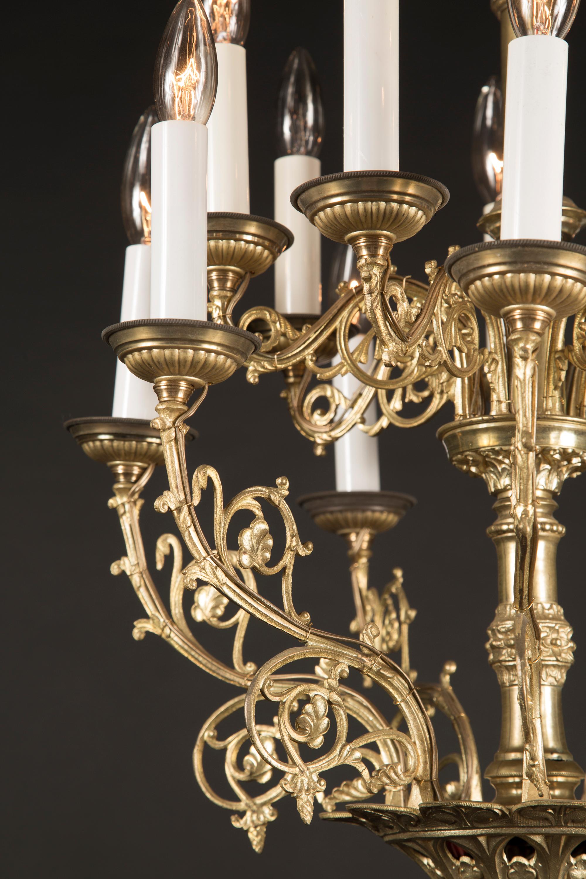 This balanced and glowing mid 20th century chandelier is cast in bronze and features details in plenty. The French fixture sports fluted bronze bobeches on each of the arms, which are separated into two tiers. The arms themselves feature scrolling