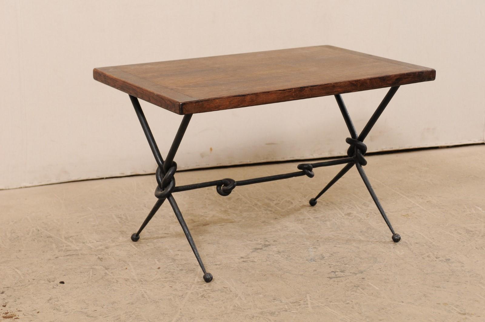 A French coffee table with a fabulously knotted forged-iron base from the mid 20th century. This vintage coffee table from France features a rectangular-shaped medium-toned wooden top, supported upon an artfully designed hand-forged iron base of