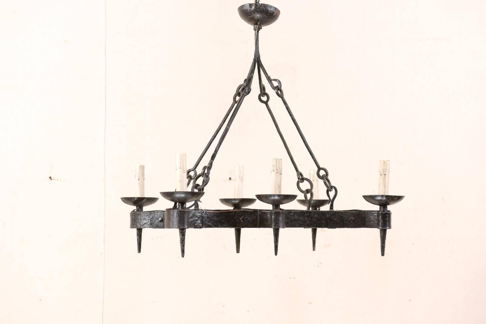 A French midcentury forged-iron six-light chandelier. This French vintage chandelier has an overall curvy, yet rectangular-shape. Six torch style lights, with iron cup style bobèches, are supported within the tightly scrolled arm extensions along