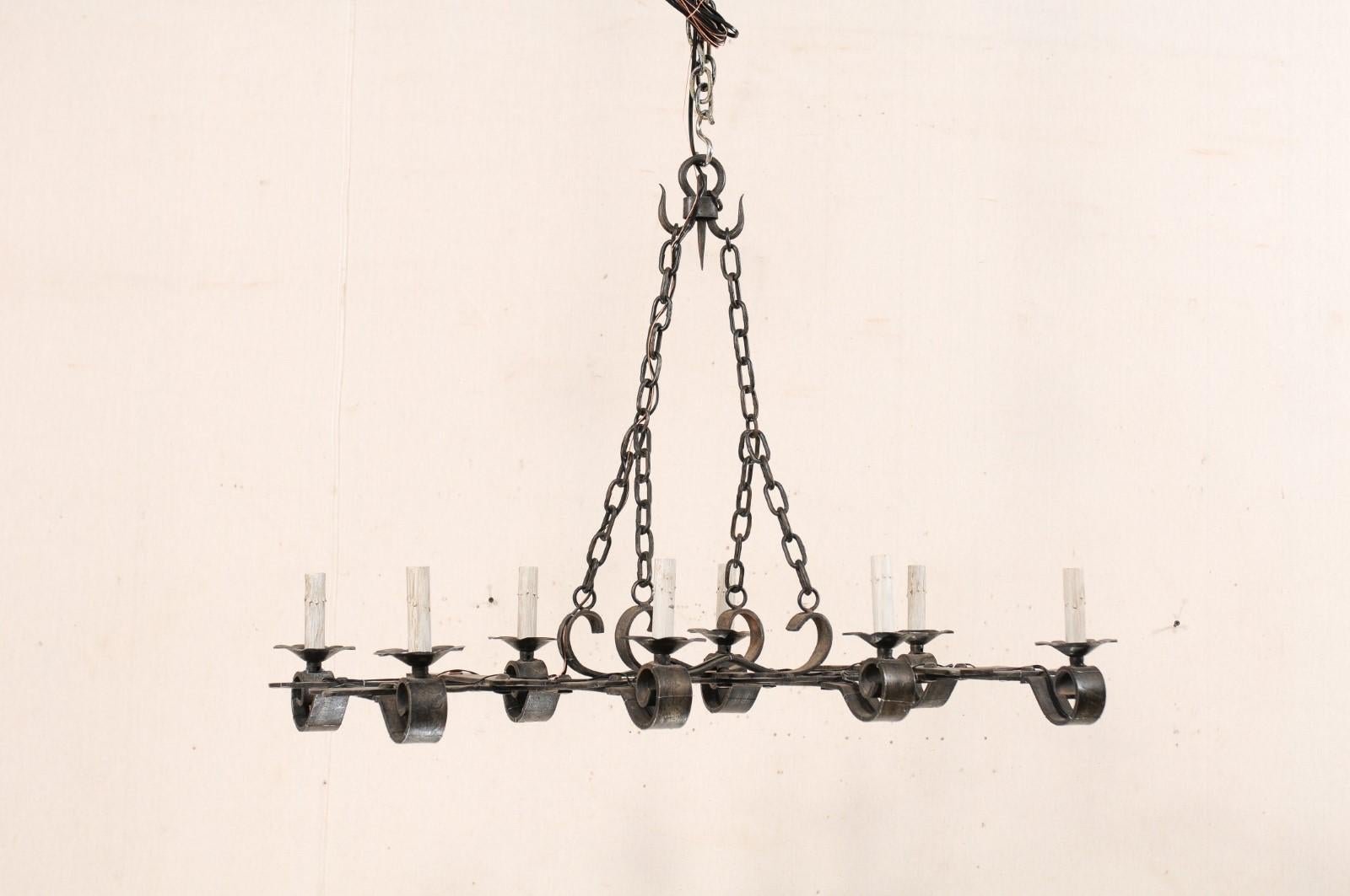 A French black forged-iron chandelier with eight-lights from the mid 20th century. This vintage chandelier from France has an overall rectangular-shape, with four cross-beams which support ruffled iron bobeches with painted candle sleeves sitting