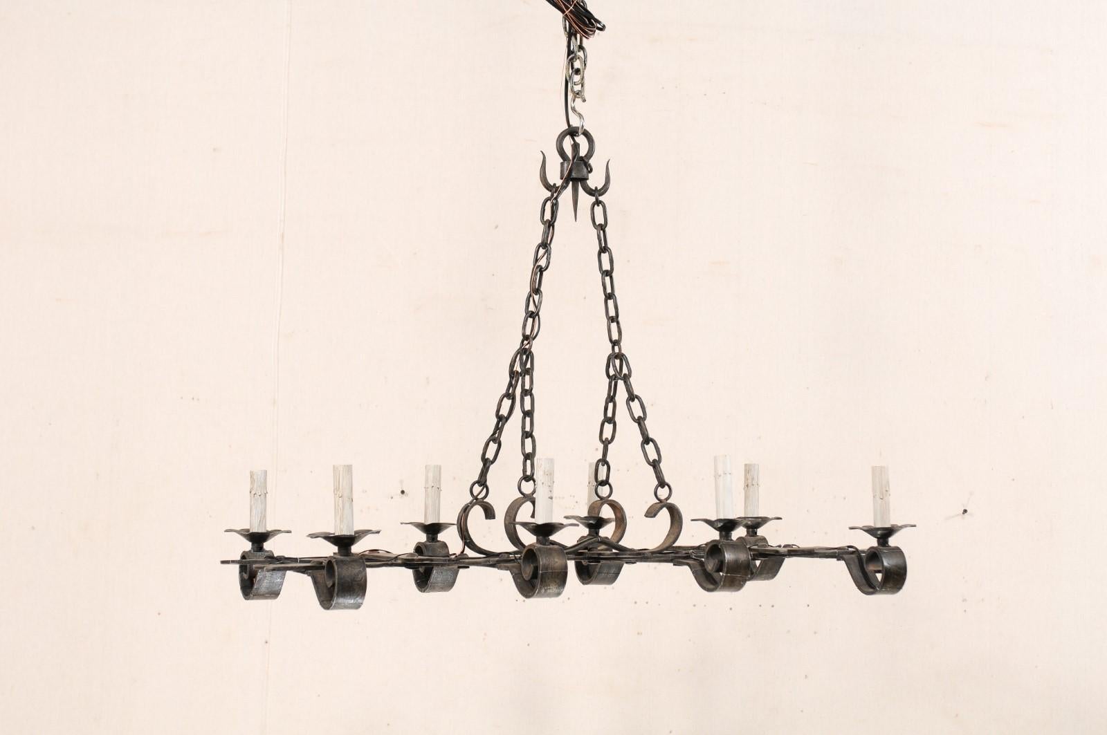 A French black forged-iron chandelier with eight-lights from the mid 20th century. This vintage chandelier from France has an overall rectangular-shape, with four cross-beams which support ruffled iron bobeches with painted candle sleeves sitting