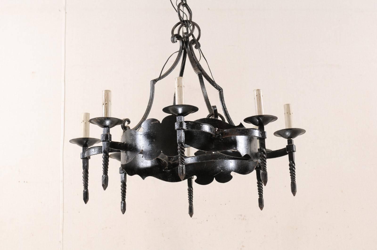 A French circular iron eight-light chandelier from the mid-20th century. This vintage French hand-forged iron chandelier features a wide central ring base with stylized cut-wave motifs along it's upper and lower edges. There are eight torch-style