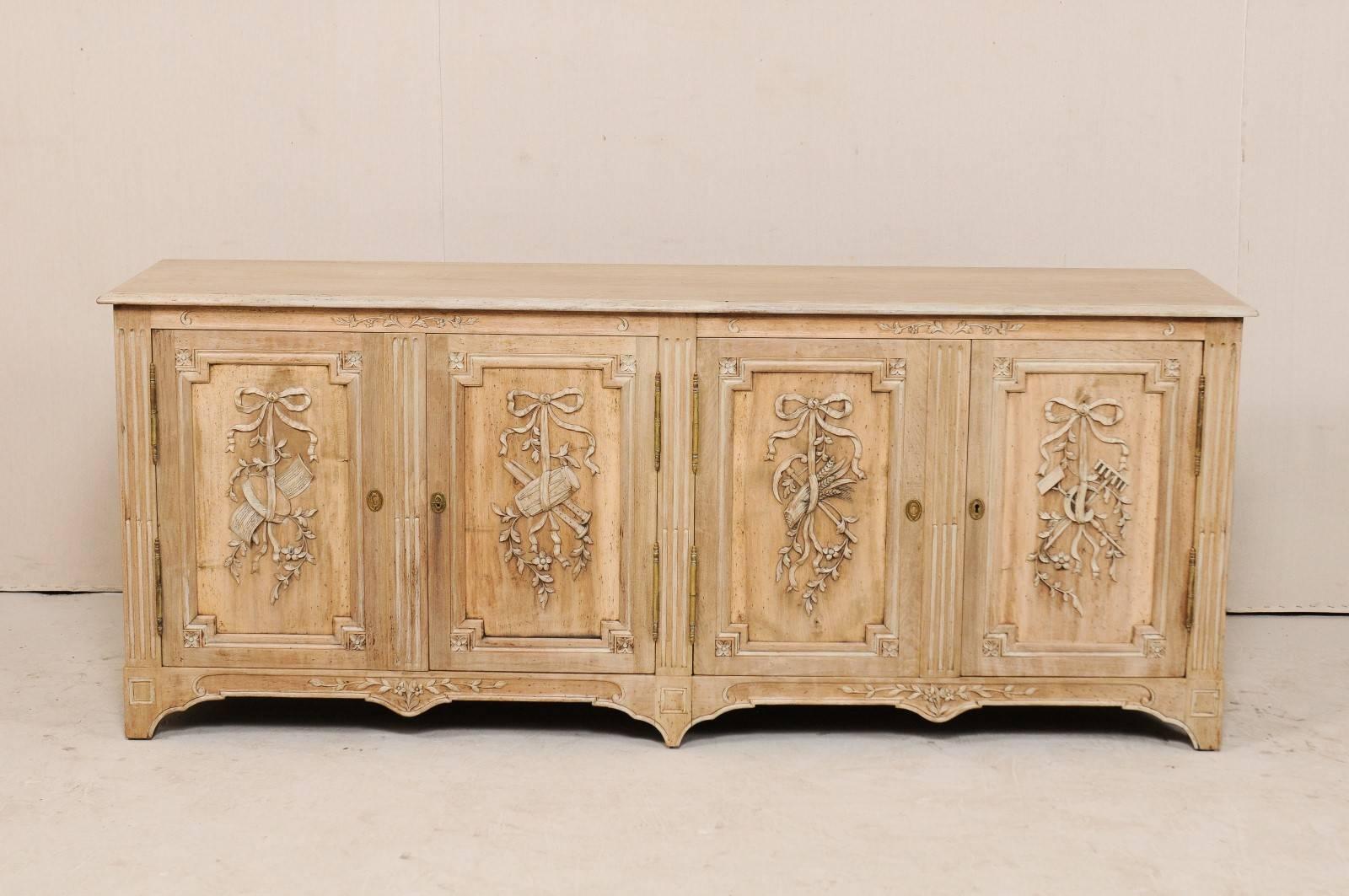 A French mid-20th century wood buffet cabinet. This midcentury French sideboard, approximately 7 feet in length, appears to tell a story with it's four delightfully and intricately decorated doors, having wood carved motifs consisting of musical
