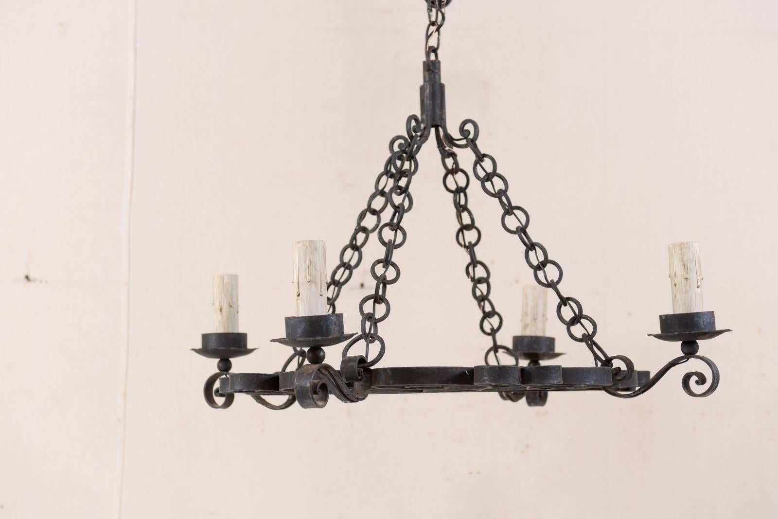 A French mid-20th century four-light forged-iron chandelier. This vintage French chandelier has an overall circular appearance, with gallery ring of this chandelier being comprised of a downward facing succession of sweetly scrolled heart-like
