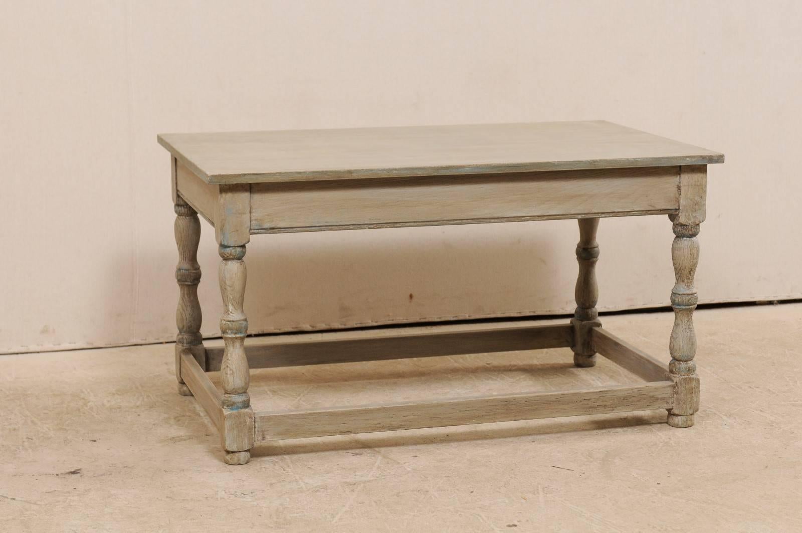 A French grey-toned wood coffee table from the mid-20th century. This vintage French coffee table of wood features a rectangular-shaped top over four nicely turned legs, each braced with a plain box stretcher between them. The skirt has clean,