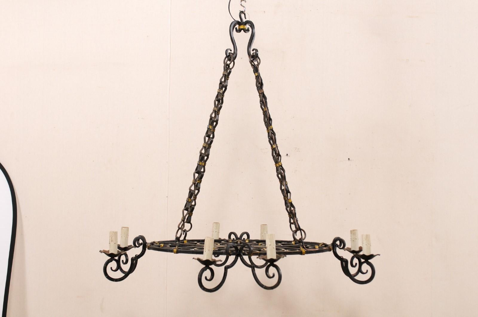 An oval-shaped French forged black iron chandelier with gold accents from the mid-20th century. This vintage chandelier from France features an oval-shaped central ring, whose profile is thin from side-view, but is elegantly adorn within it's center