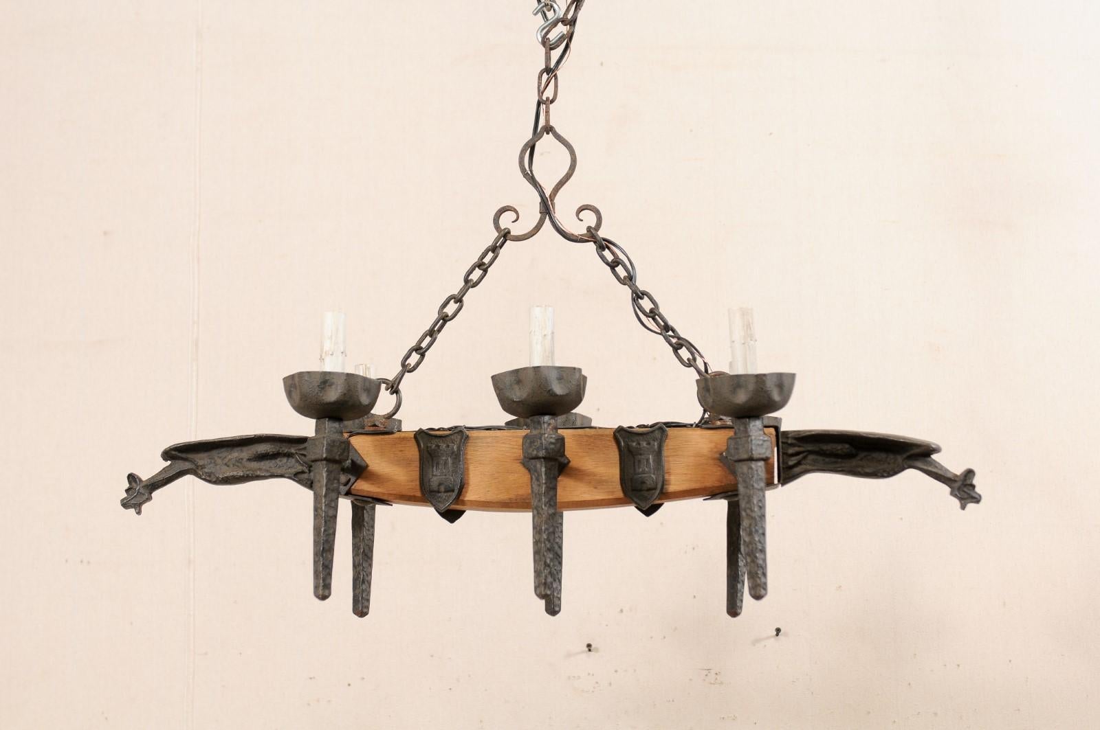 A French six-light wooden and iron chandelier with gargoyle motif from the mid-20th century. This vintage French chandelier has a central wooden beam with six torch-style iron arms, three at each opposing side. A pair of gaping mouthed, alert iron
