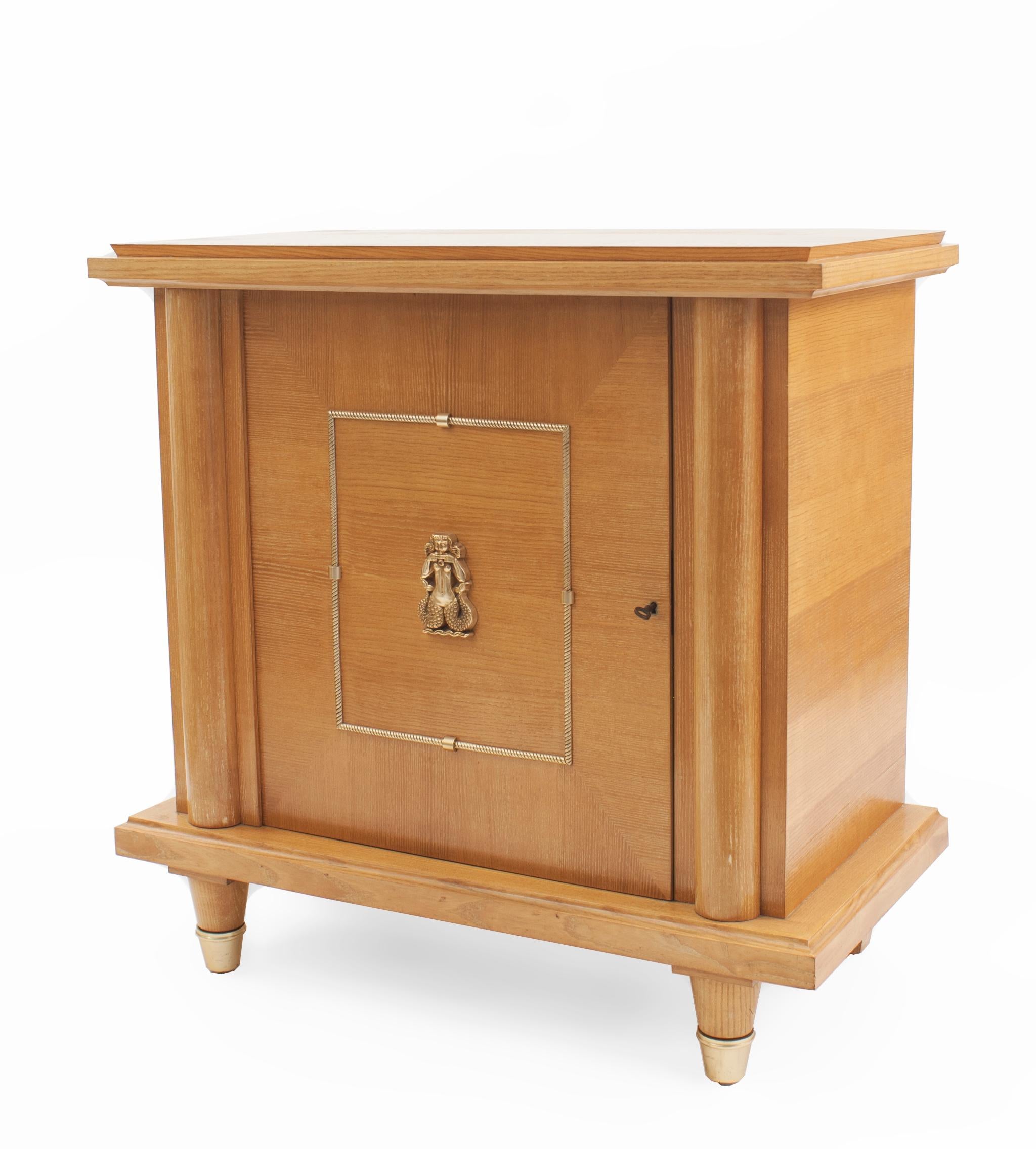 French Mid-Century (1940s) sycamore commode / bar with column sides & a single front door having a gilt metal rope design centering a medallion figure (attributed to MAISON MERCIER FRERES).
