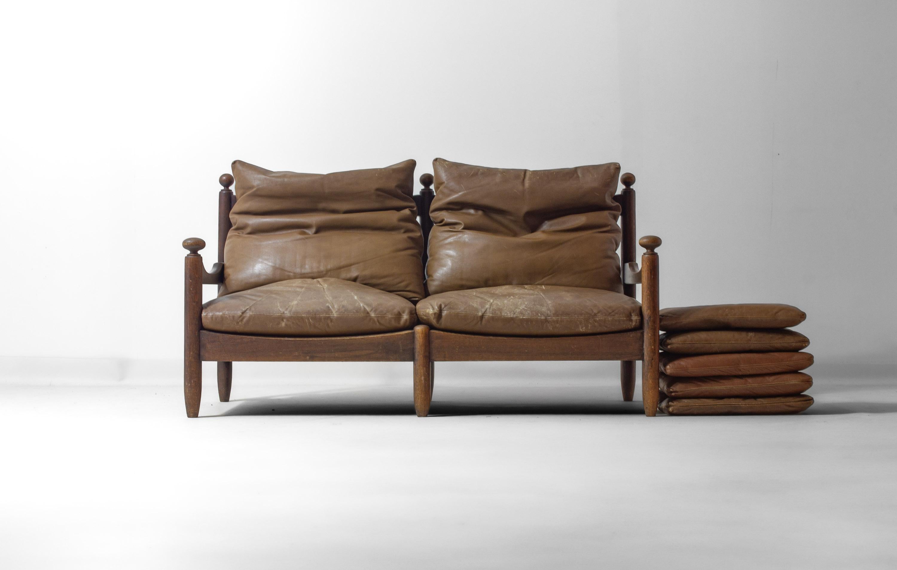 Divano a due posti realizzato in Francia negli anni '50. Il divano ha una struttura in rovere massiccio con finitura scura e presenta terminali arrotondati, braccioli curvi e schienale a doghe. I cuscini sono realizzati in pelle spessa e di alta