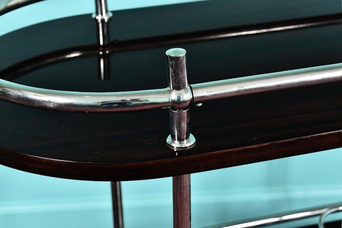 French midcentury bar cart or serving cart in palisander

 Oval veneer wood top tray rests above a smaller oval shaped base tray. The cart is held together with chrome tubing supports, which also utilized as rails and shaped into glass or bottle