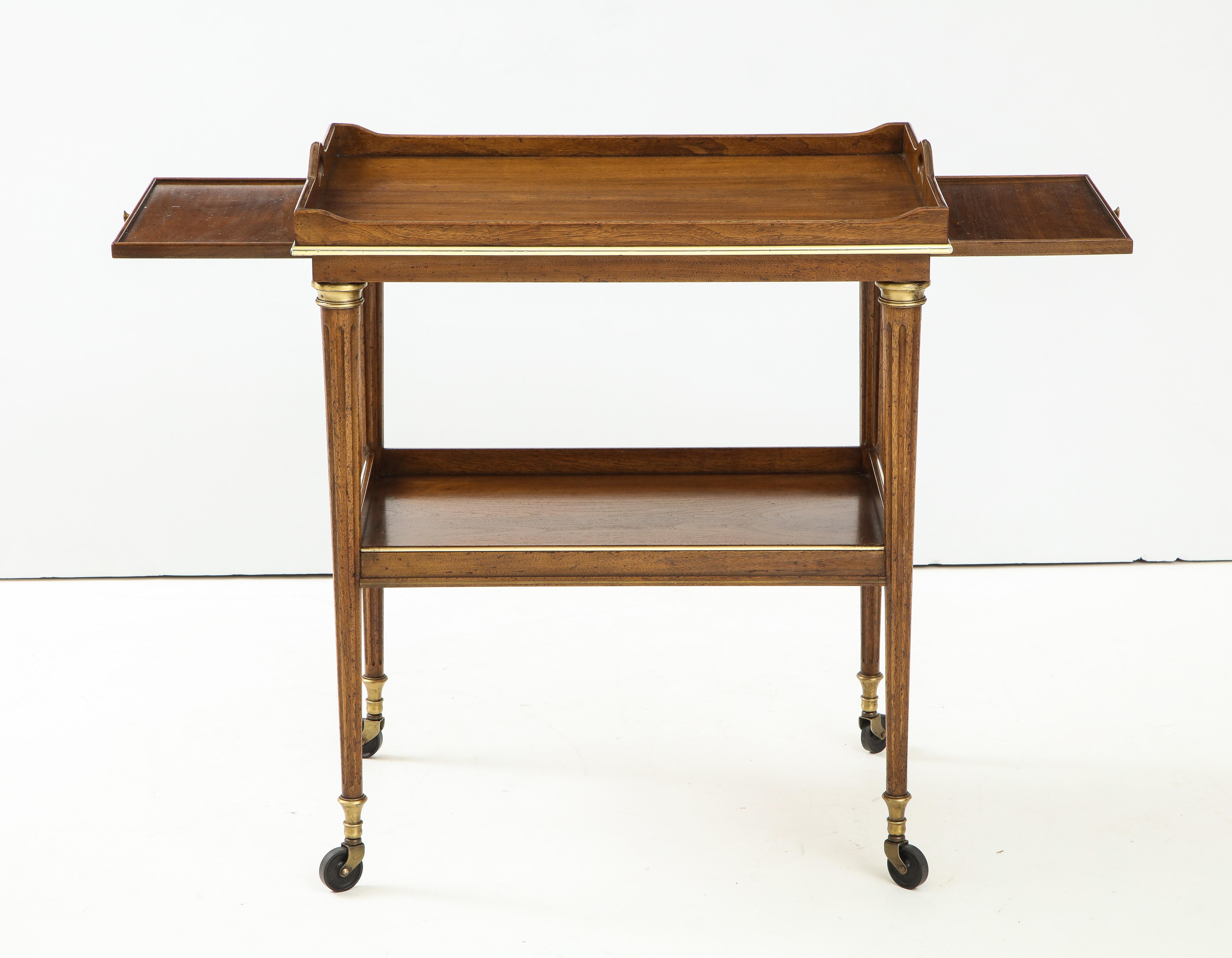 A French two tear light mahogany bar trolley with brass accents. This chic and unique piece has reeded tapered legs on castors and two pullout trays. It's small scale makes it ideal for any space or occasion!