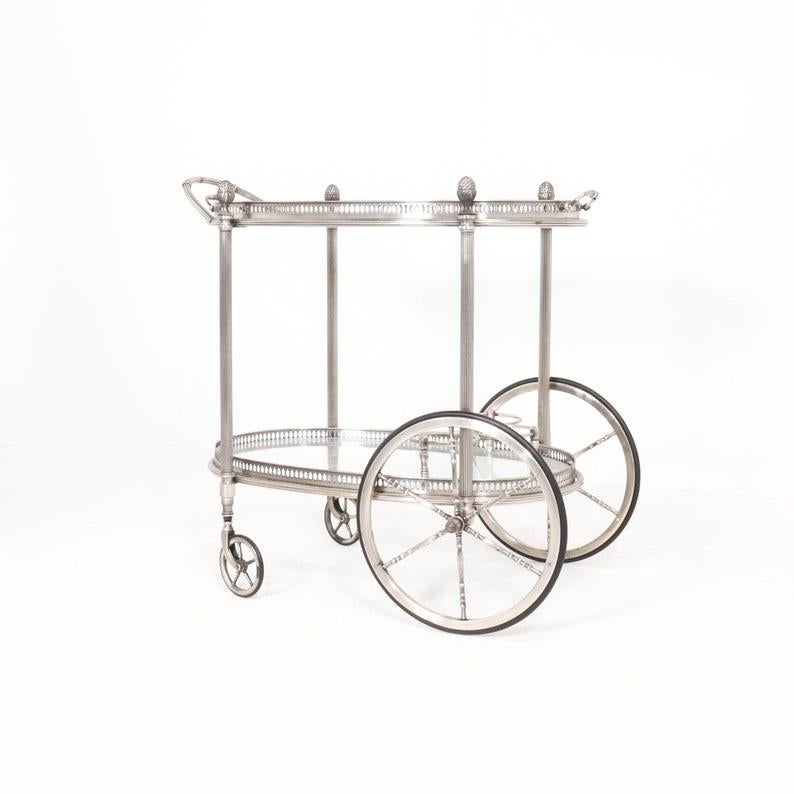 Original French serving trolley in neoclassical style, attr. to Maison Baguès.
This serving trolley has clear glass and a heavy polished metal frame with fine classical details such as pine cones, scrollwork, etc.
The two trays have a punched out
