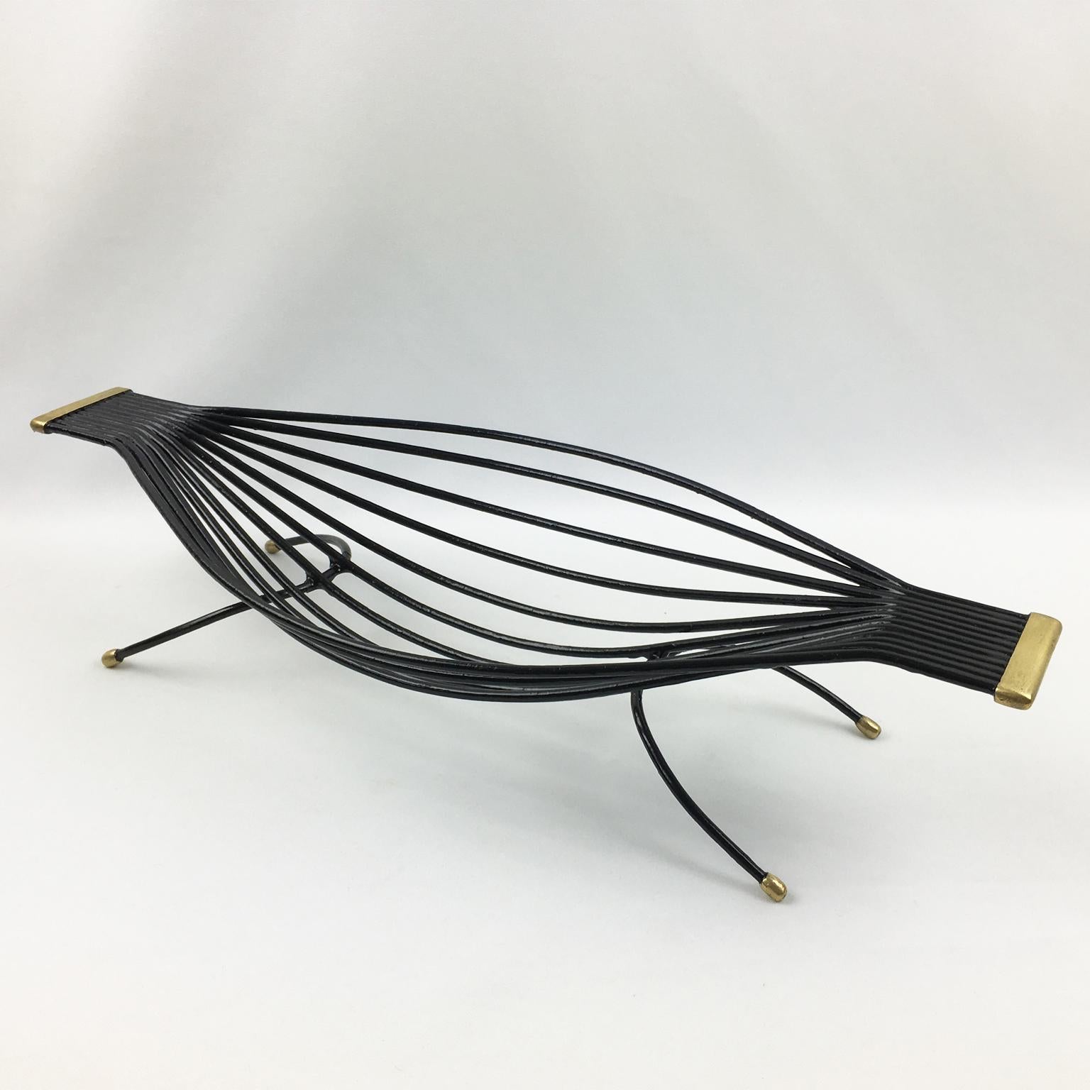 This lovely 1960s modernist metal fruit bowl, basket, or decorative centerpiece has an original black paint patina with polished brass feet and handles. The elongated hammock shape has a zoomorphic flair with thin metal rods. There is no visible