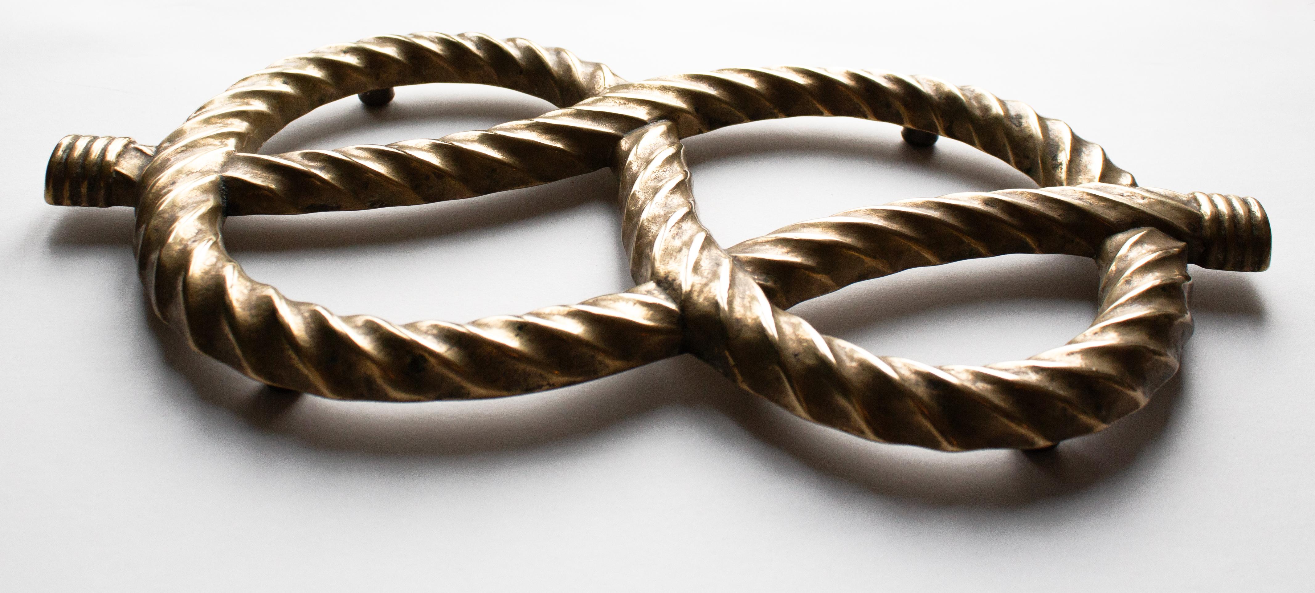 Questo elegante e grazioso sottopentola francese in ottone presenta un motivo a corda splendidamente scolpito, intrecciato in un design fluido e simmetrico. Il pezzo è fuso in ottone massiccio con una patina calda e invecchiata che mette in risalto