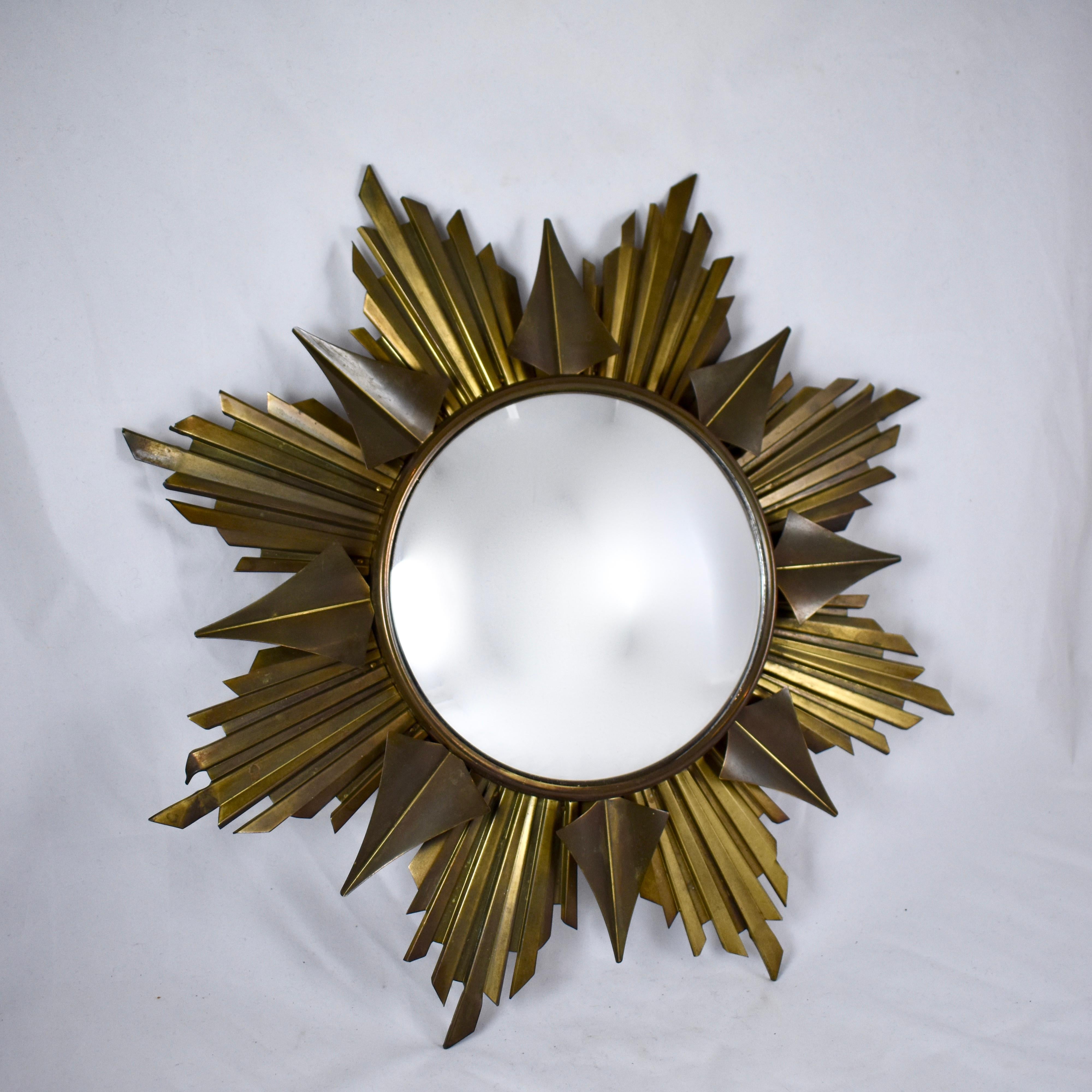 An elegant and dimensional French, Mid-Century Modern Era polished brass sunburst wall mirror. Eight pleated and fluted sun rays back eight arrow shaped rays and extend from a wide bezel framing a convex, round mirror. Each ray attaches to the bezel