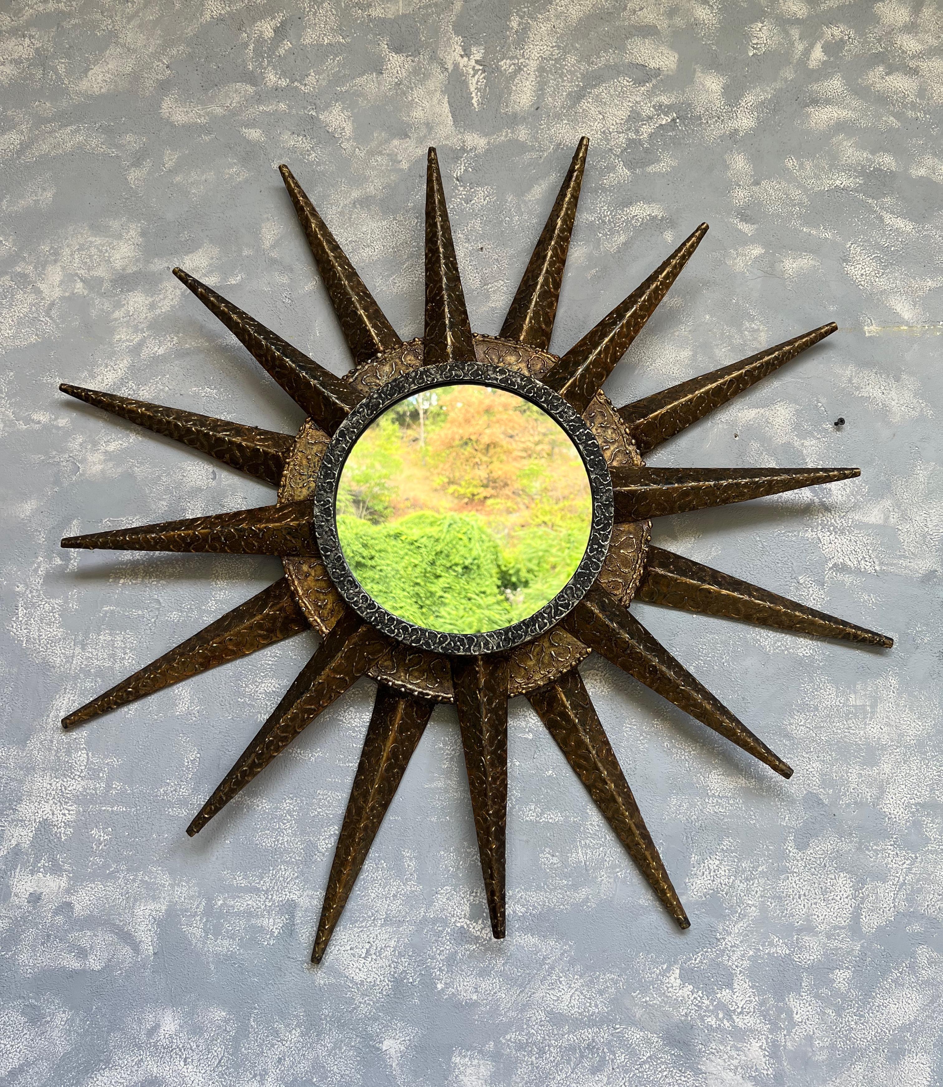 This dynamic French mid century modern sunburst mirror in the “brutalist” style features a double tiered central frame. The exterior part consists of 8 spikes in a rich gilt finish and the interior part has 8 spikes connected to a more silvered gray