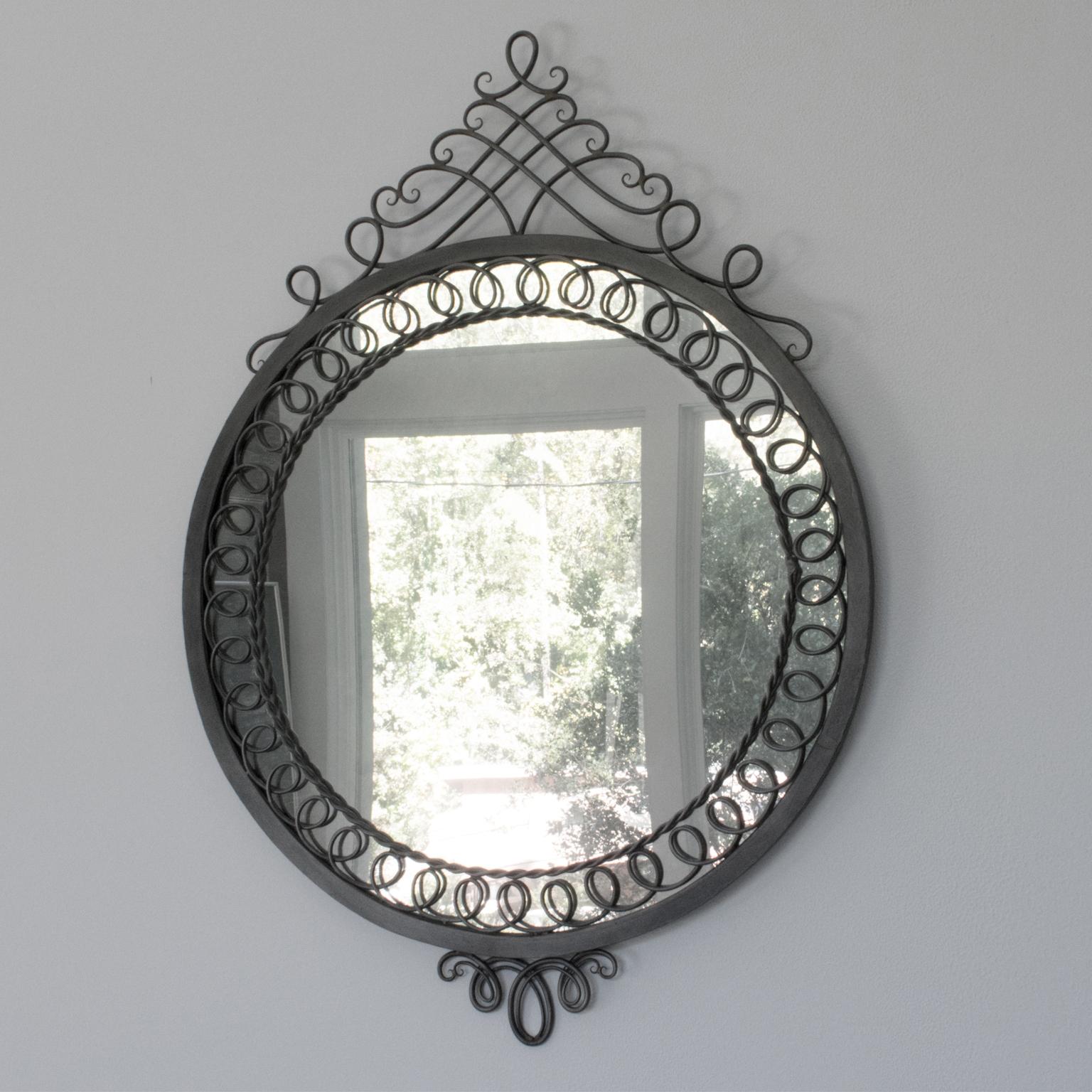 This striking French 1950s Mid-Century neoclassic cast iron wall mirror is a timeless piece of home decor. Its impressive rounded shape is surrounded by ornately detailed metal framing, finished with a beautiful original gunmetal patina. The lack of