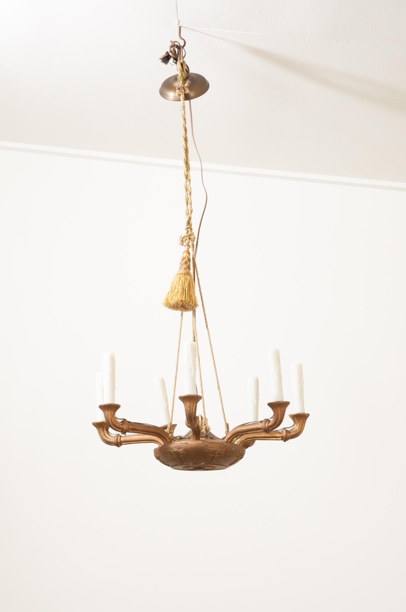 A wonderfully unique chandelier crafted in France in the Empire style. This wonderful chandelier is not very heavy and made of carved wood, it’s supported with golden rope and adorned with a gold tassel. Seven arms hoist new white faux melting wax