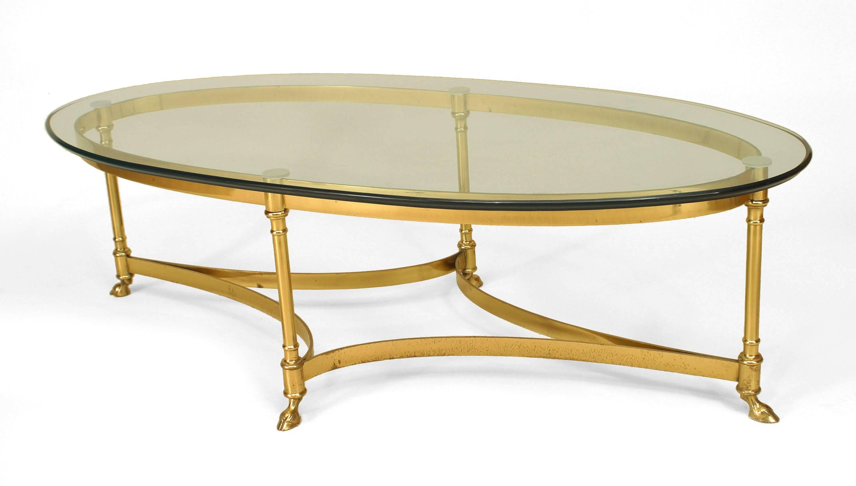 French Modern design oval brass coffee table with a glass top and stretcher over small hoof feet. (attributed to LA BARGE)
