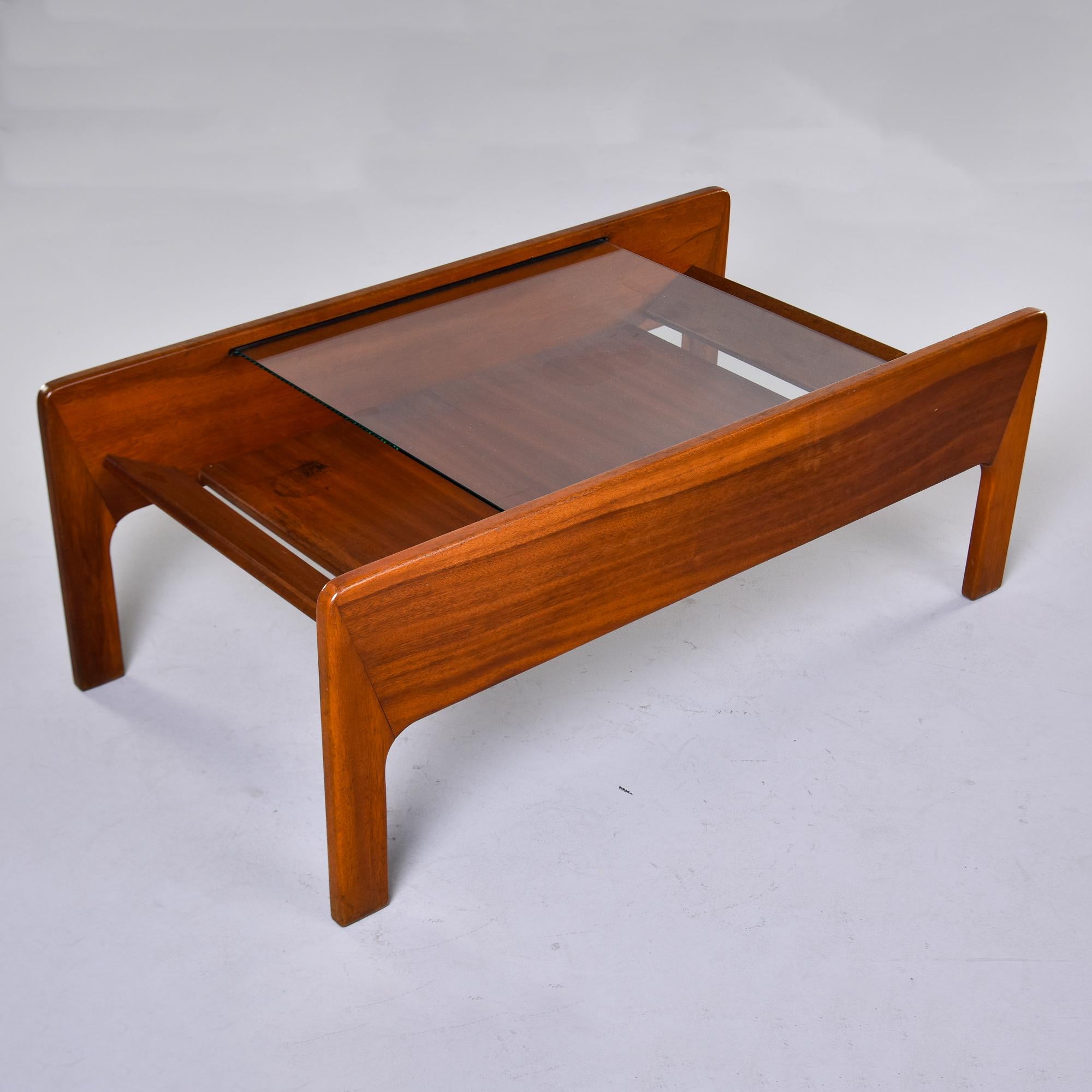 Found in France, this unusual coffee or cocktail table dates from the 1960s. We believe this is made of teak, with a base featuring prominent, curved corners where the legs meet, and a lower wood shelf flanked by angled, separated wood end pieces.