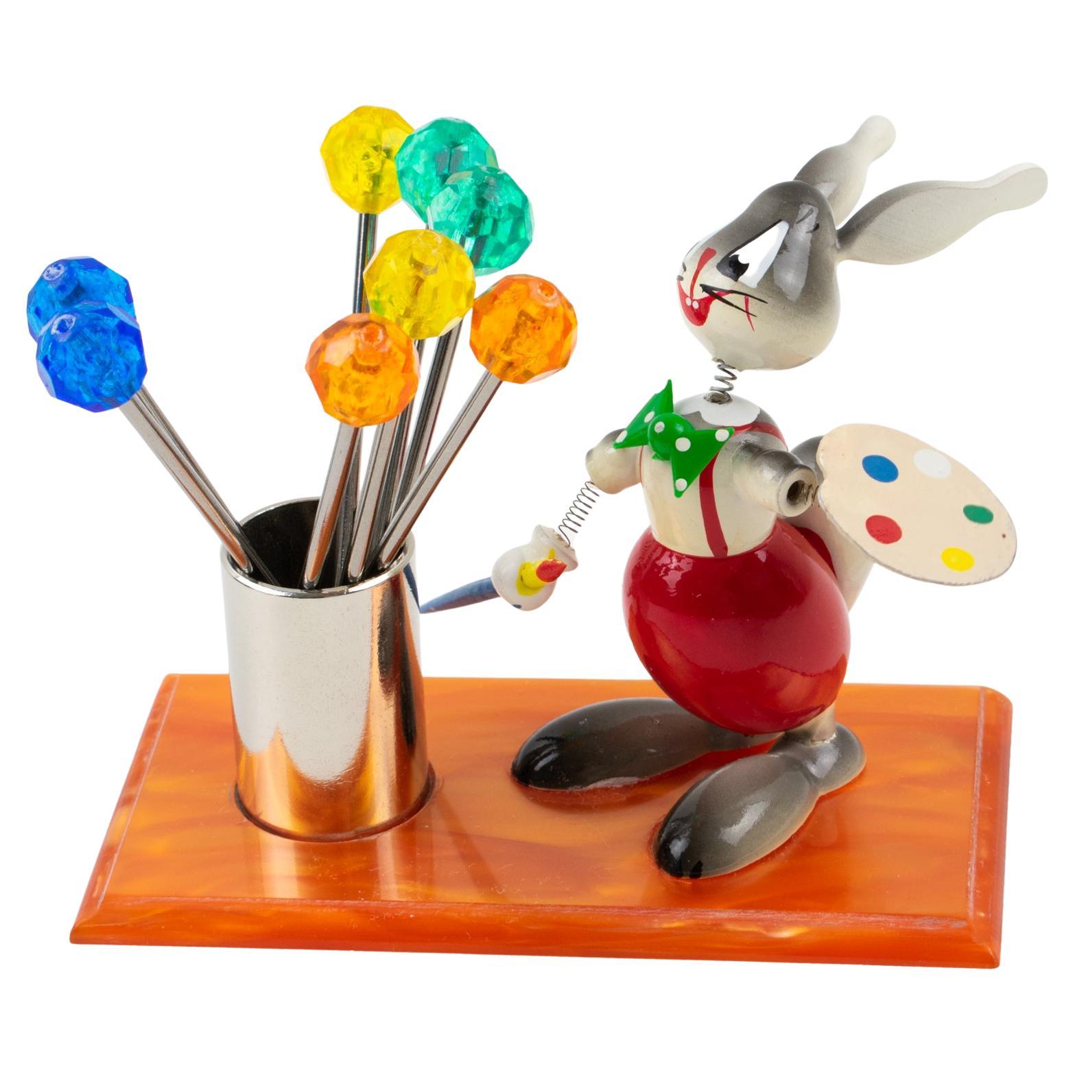 This is a cute French Mid-Century bar accessory cocktail pick set. This little guy is probably not Picasso, but he will be a great conversational piece for your next party with friends !!
The bar set includes a wooden bunny painting next to a