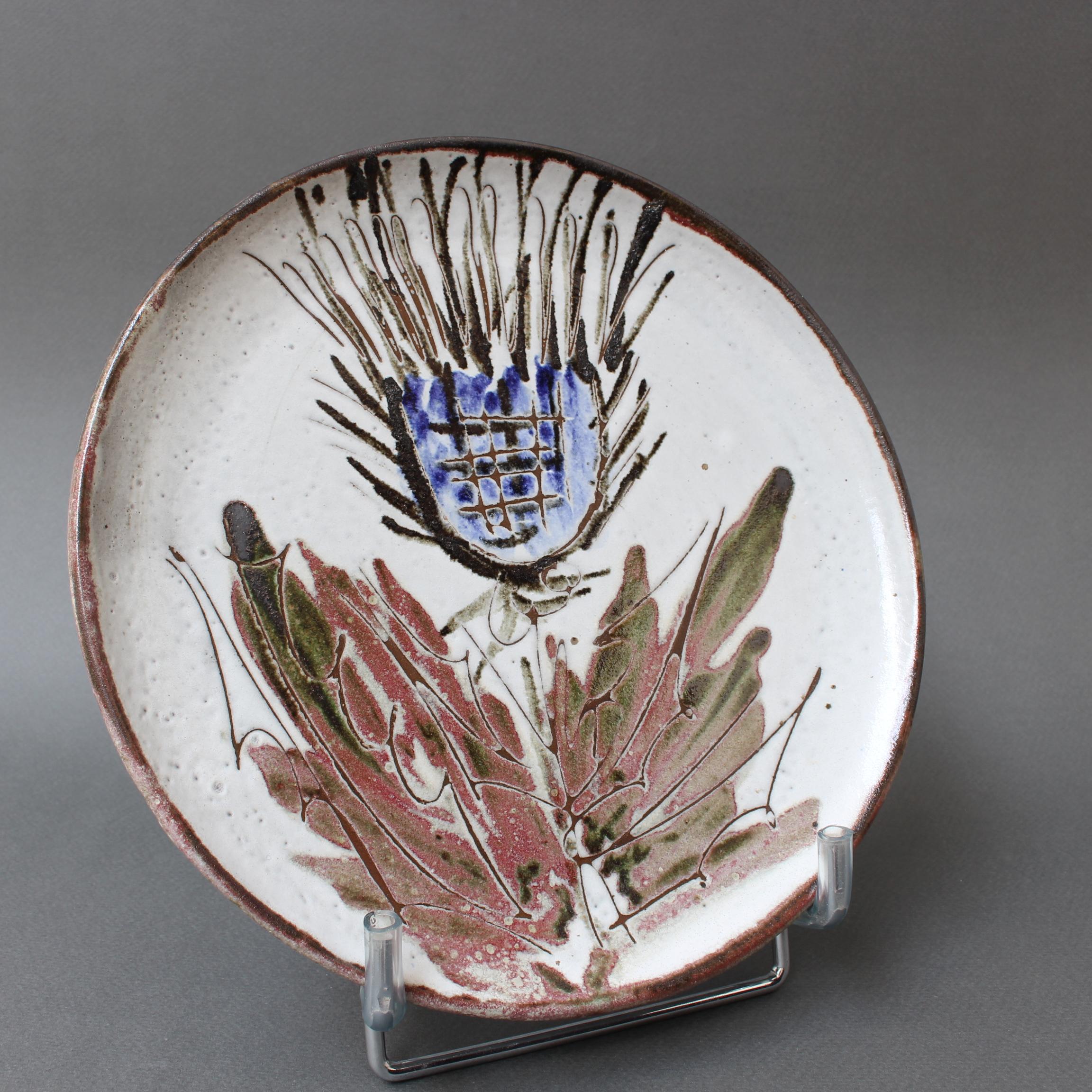 Mid-century decorative plate (circa 1960s) by Albert Thiry. A chalk-white glaze provides the background for a colourful thistle motif in the centre recess of this piece of ceramic. The incised plant has depth and adds a tactile element to the piece.