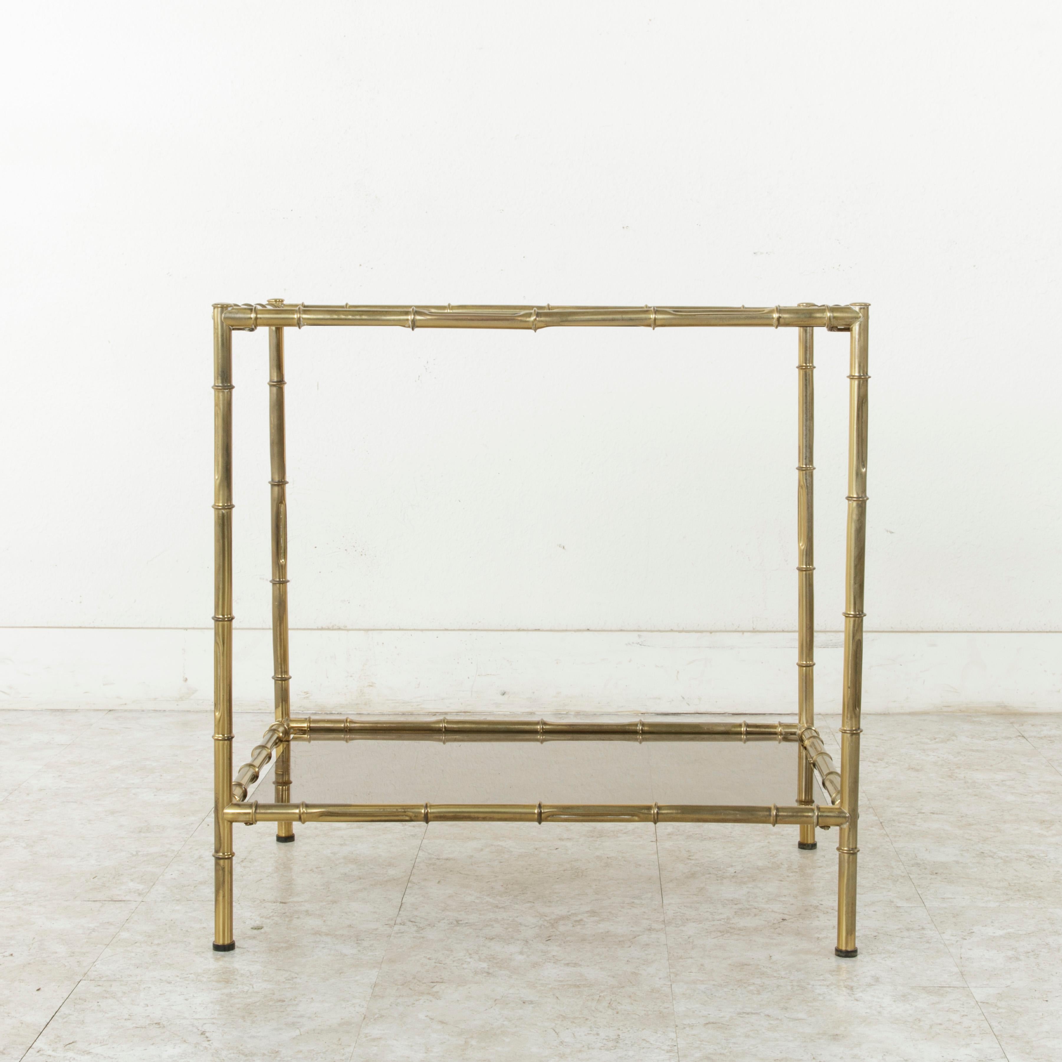 This mid-20th century French faux bamboo brass side table features an upper and lower shelf fitted with smoked glass. Its bamboo detailing includes indentations which imitate the growing pattern of the plant. A versatile serving piece that could