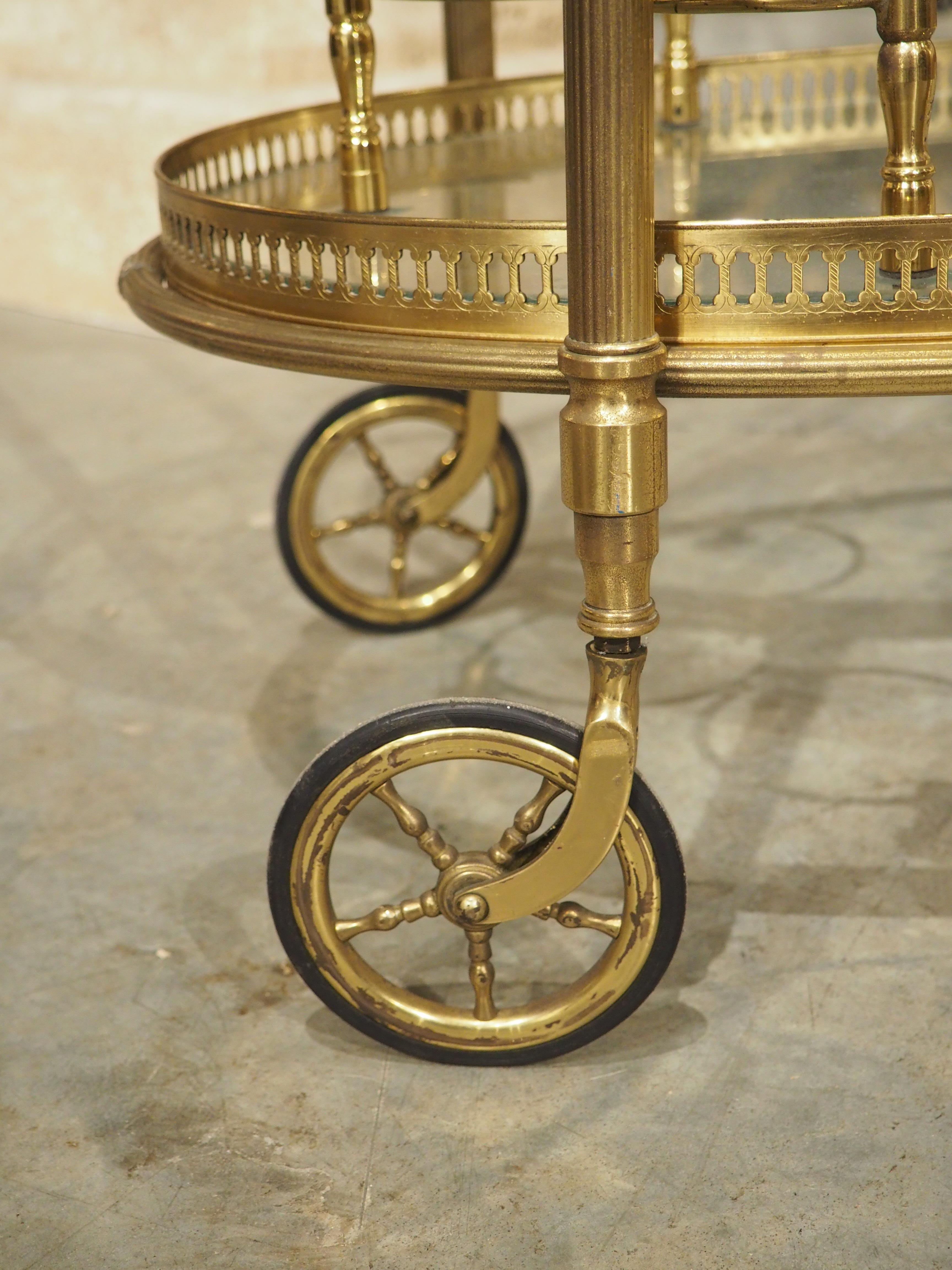 Attributed to Maison Baguès in Paris, this functional bar cart features two tiers of glass set inside a gilded brass frame. Beaded handles on the removable top tier allow the 14 W x 26 7/8 tray to be used for drink service. The bottom tier has three