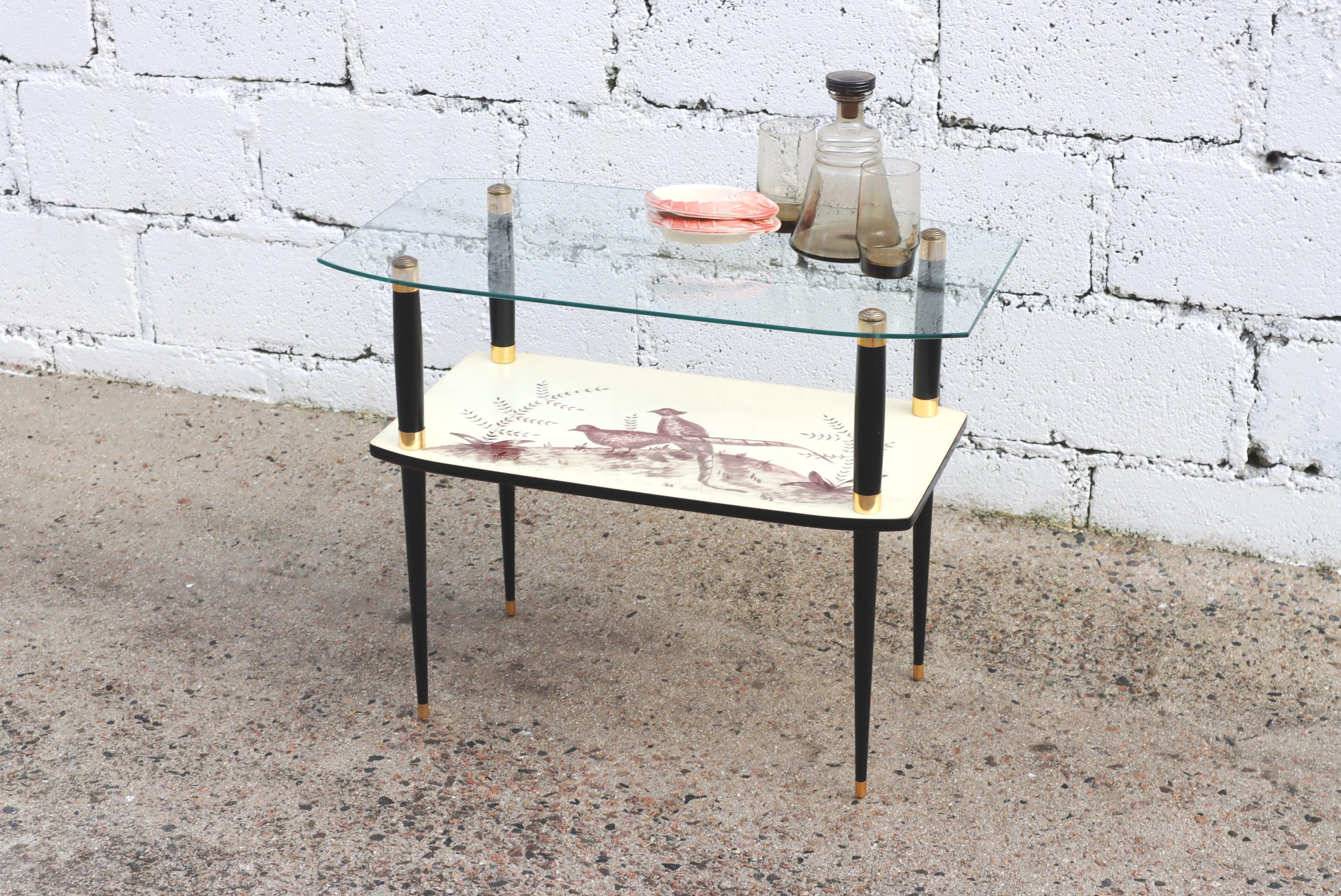 Charming Mid-Century Glass Formica Console Table from the 50s

Slender piece of Furniture with a slightly rounded Glass Top.

The lower Shelf made of Formica is decorated with a Pheasant Motif

in earth Colors on ecru-colored Underground.

Slim legs