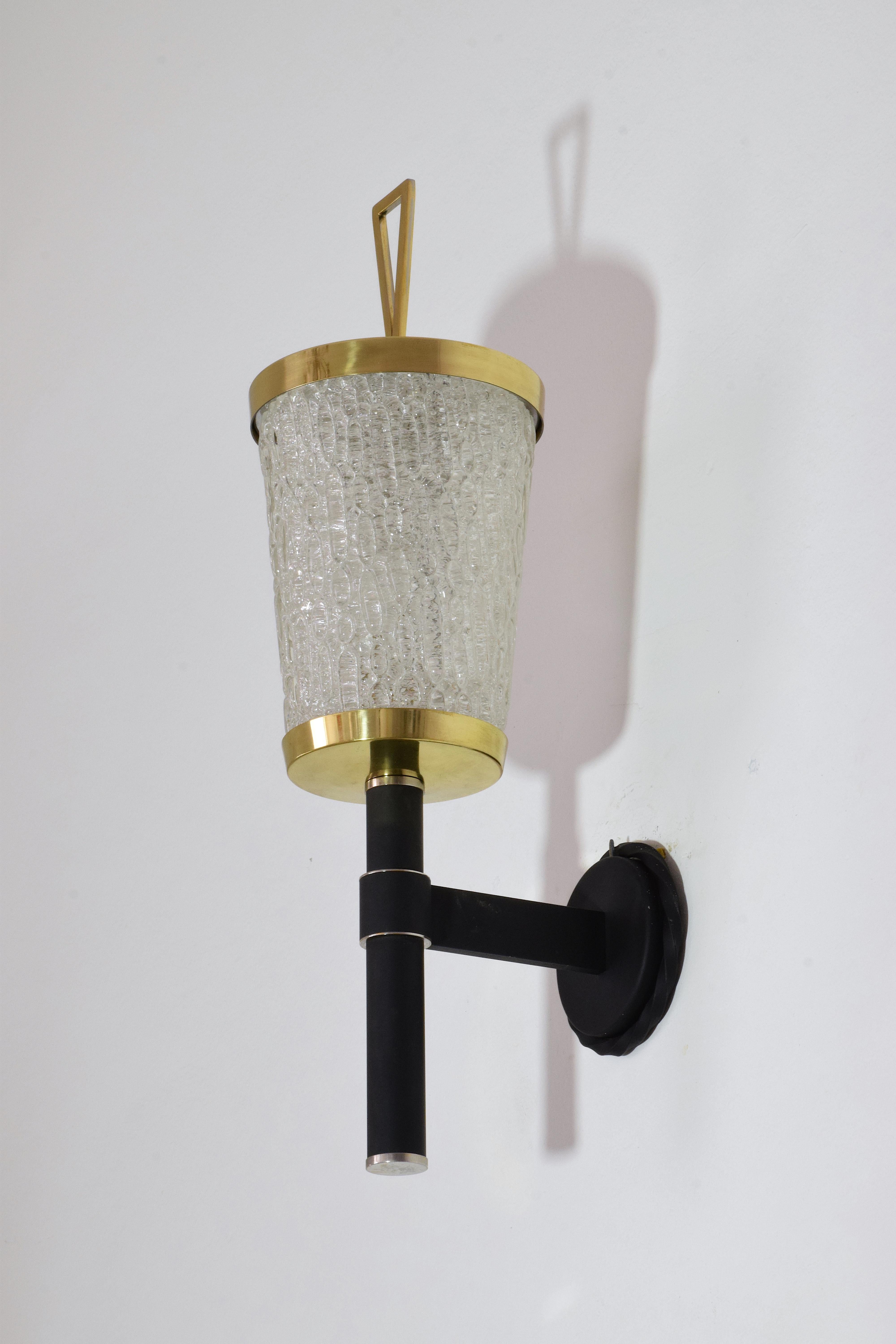 A 20th Century vintage sconce or wall light by French lighting manufacturer DLG Arlus, circa 1050s designed with textured glass, polished gold brass details and a black structure.
France, circa 1950s.